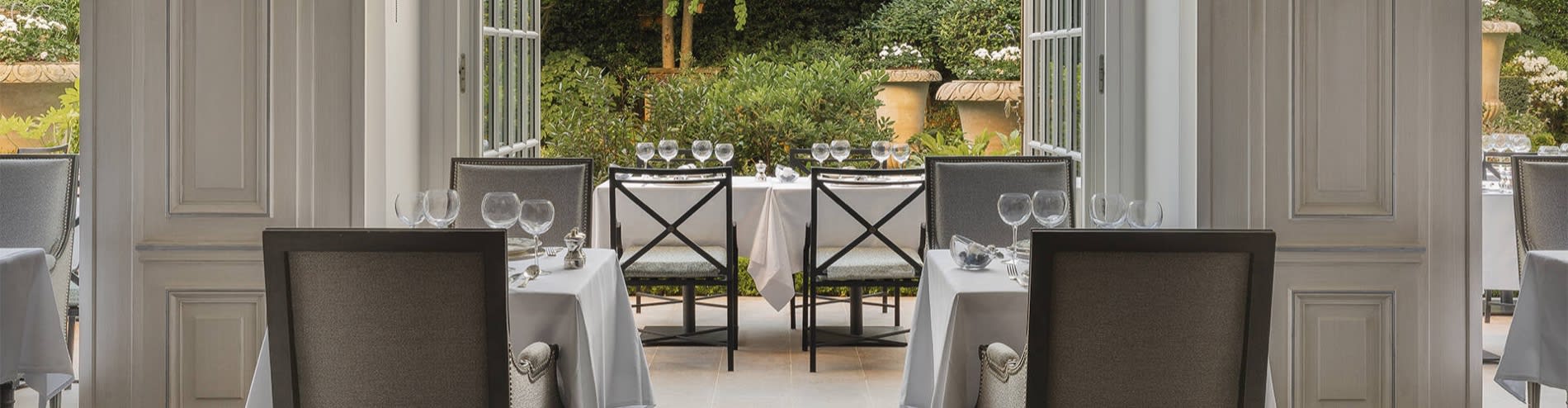 Tables nappées de blanc de Maison Roland, le bistrot du jardin du Shangri-La Paris, sous les arbres de l'avenue d'Iéna