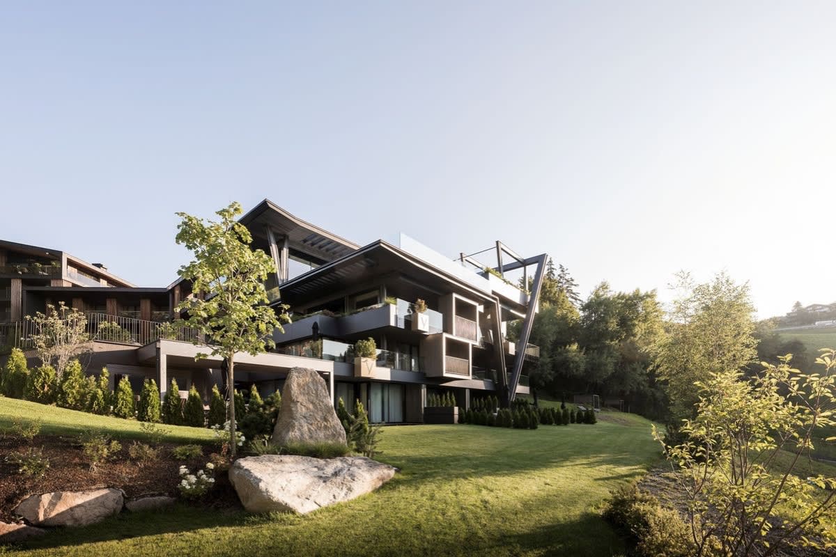 Wooden facade of the Viktoria Alpine Hideaway in Hafling, V-shaped structure, balconies and sun-drenched sloping garden