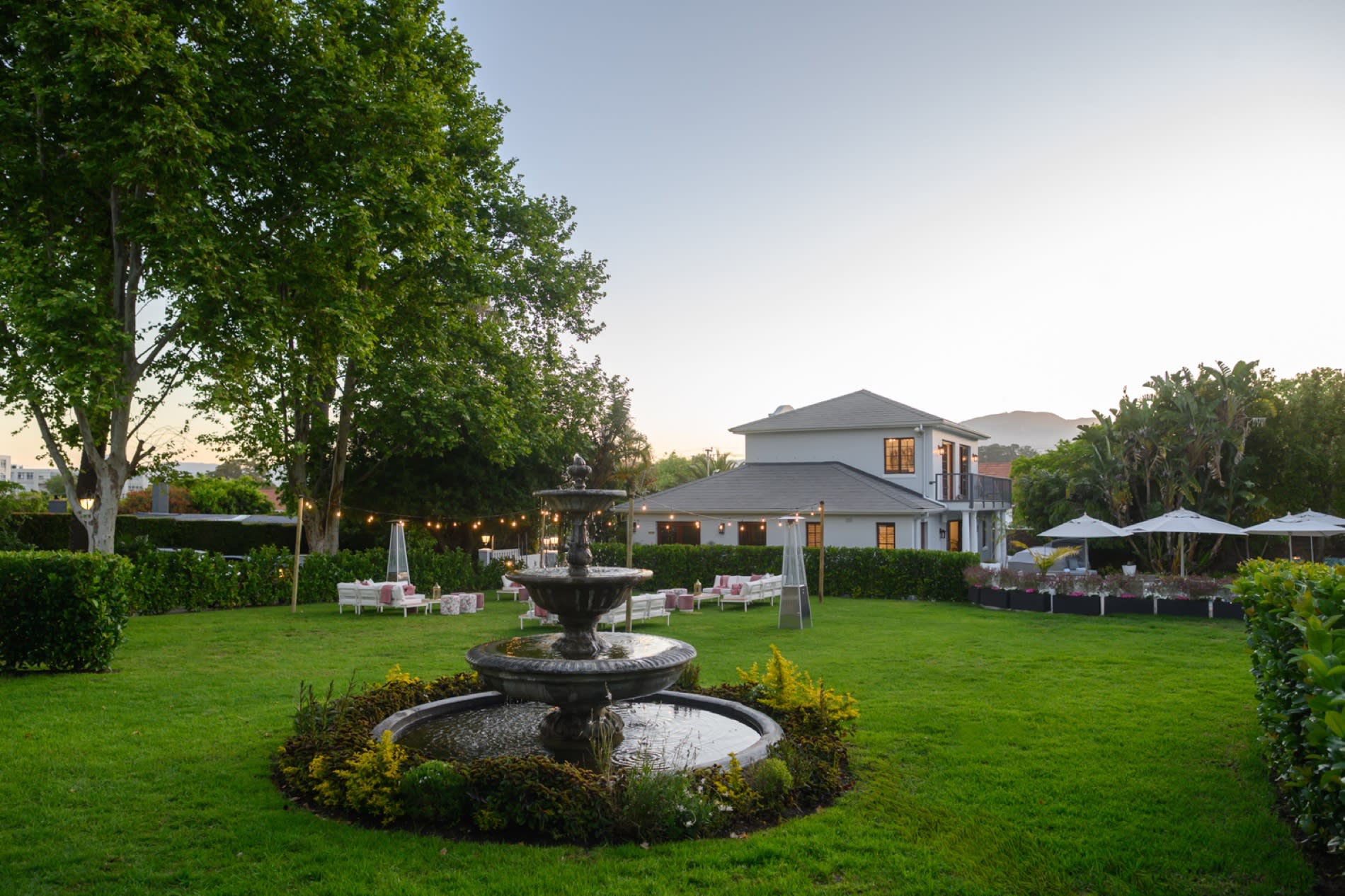 Grande pelouse du Palm House au Cap, fontaine en pierre et tables de jardin dressées pour un dîner sous les arbres