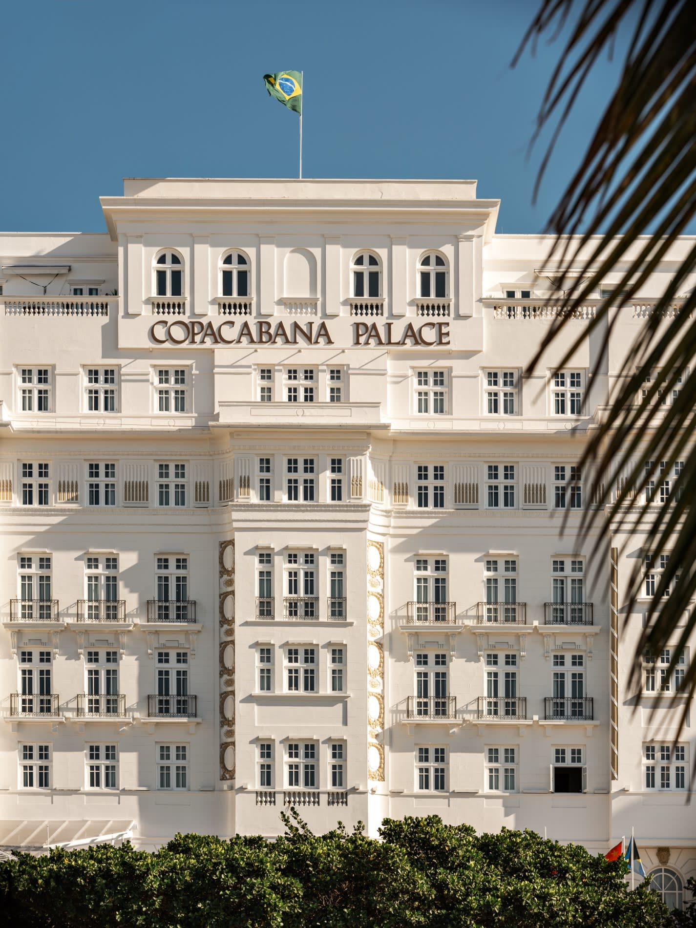 Frontón blanco del Copacabana Palace en Río de Janeiro, letras doradas y bandera brasileña bajo una palmera