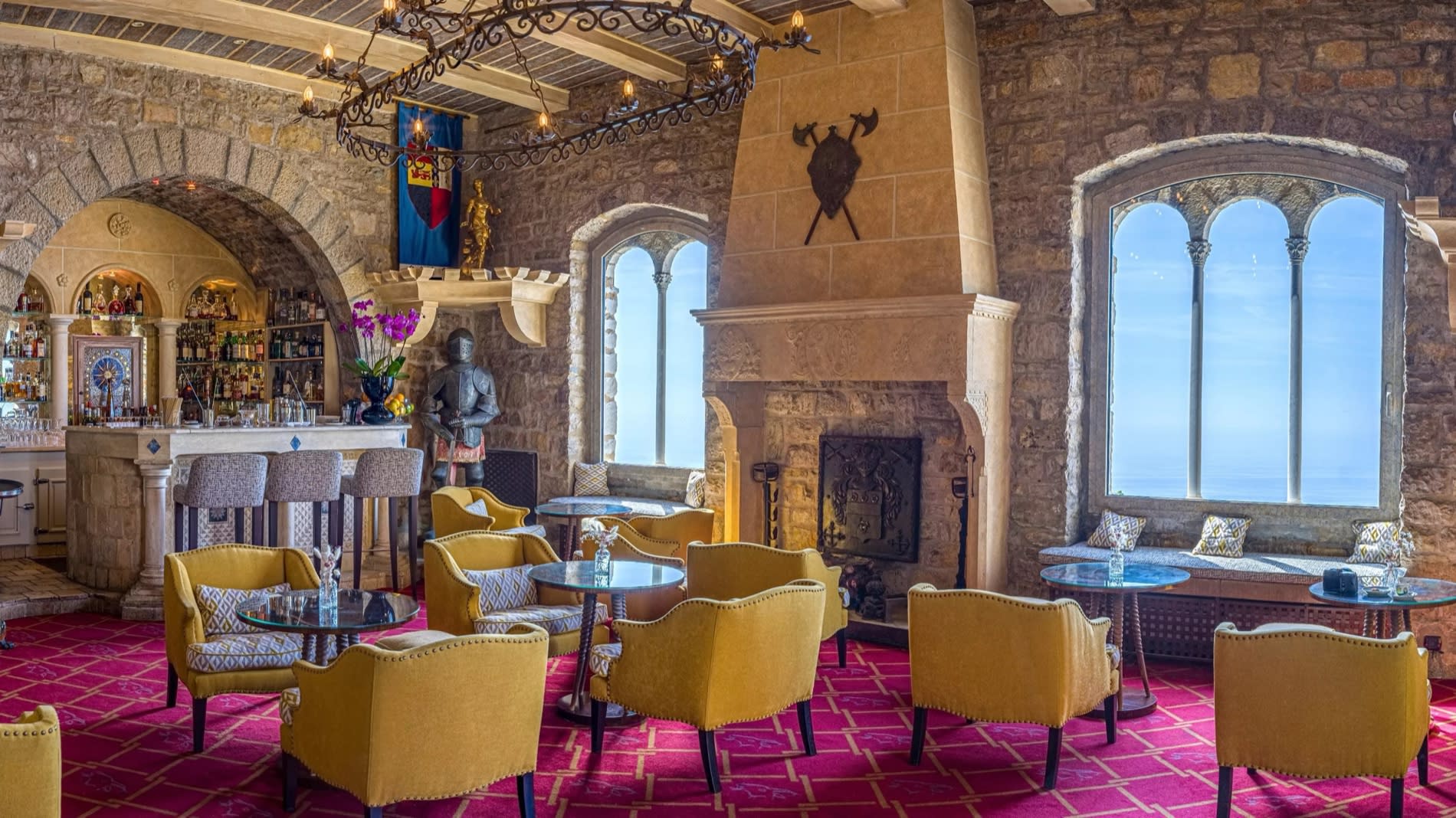 Bar at Château de la Chèvre d'Or in Èze, featuring stone vaults, a fireplace, and yellow armchairs