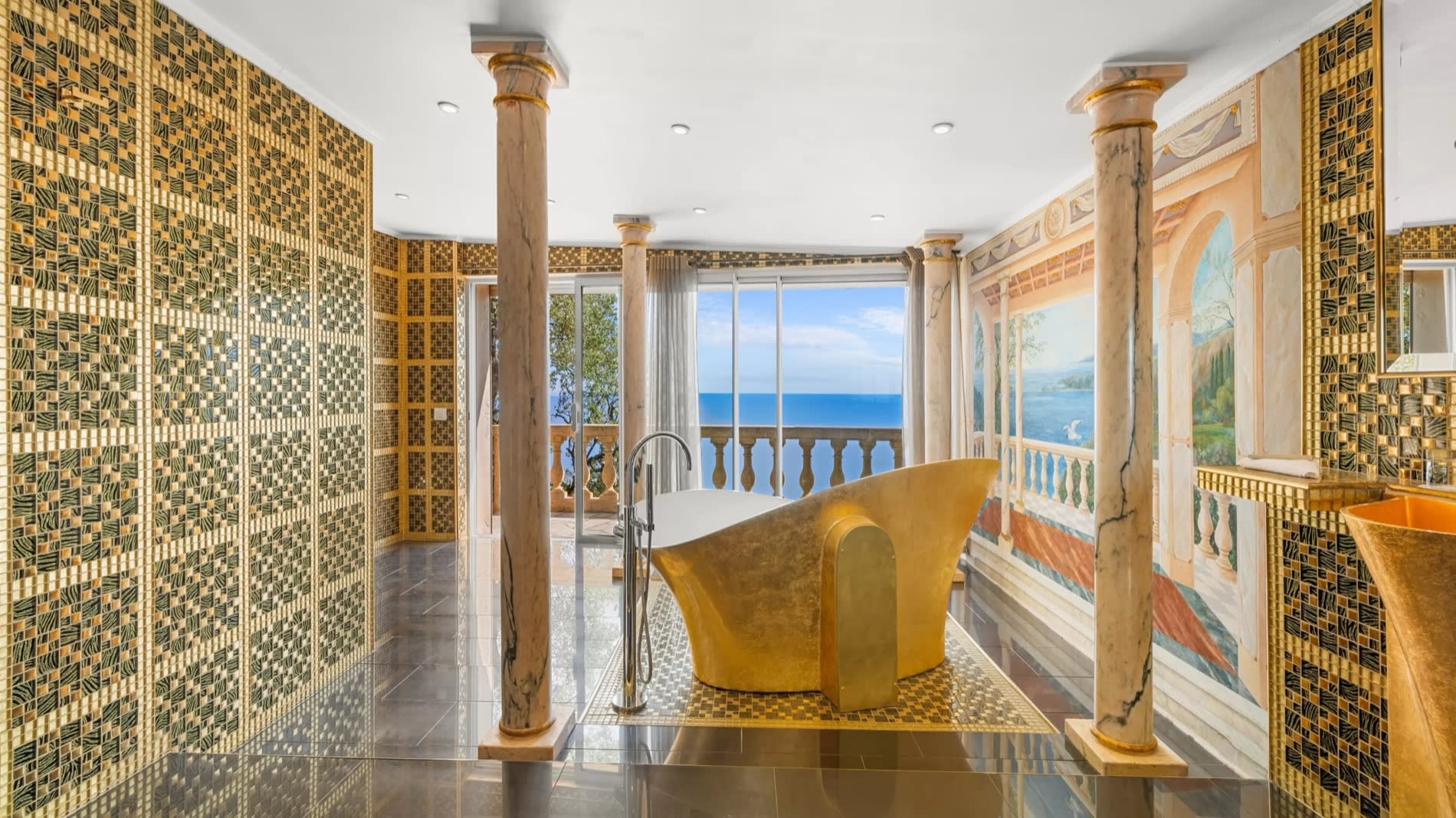 Golden bathroom in a suite at Château de la Chèvre d'Or in Èze, with bathtub, columns, and fresco