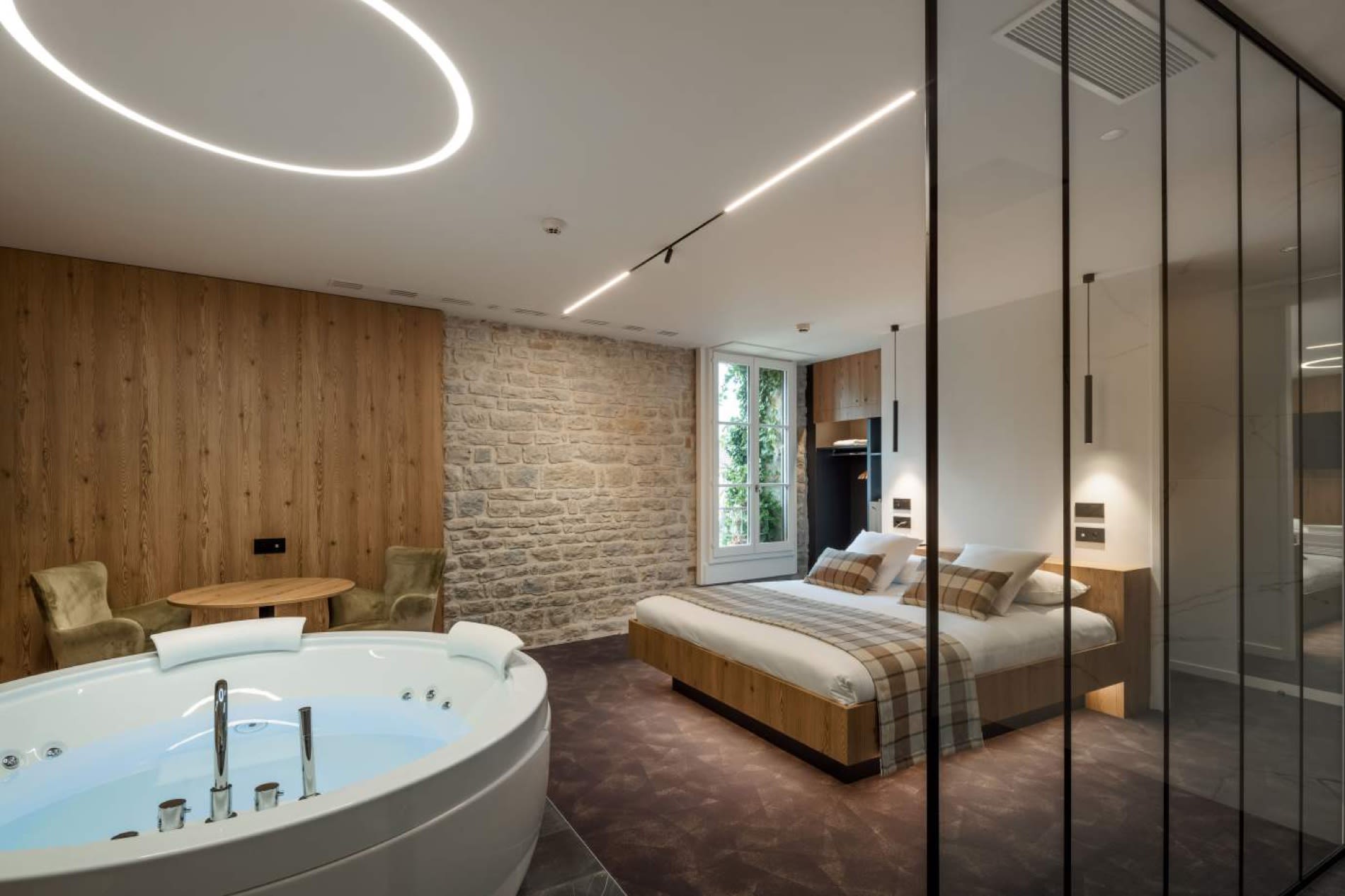 Une chambre Deluxe de l'Hôtel Spa Parenthèse avec sa baignoire balnéothérapie ronde et son mur de pierre, à Chille près de Lons-le-Saunier