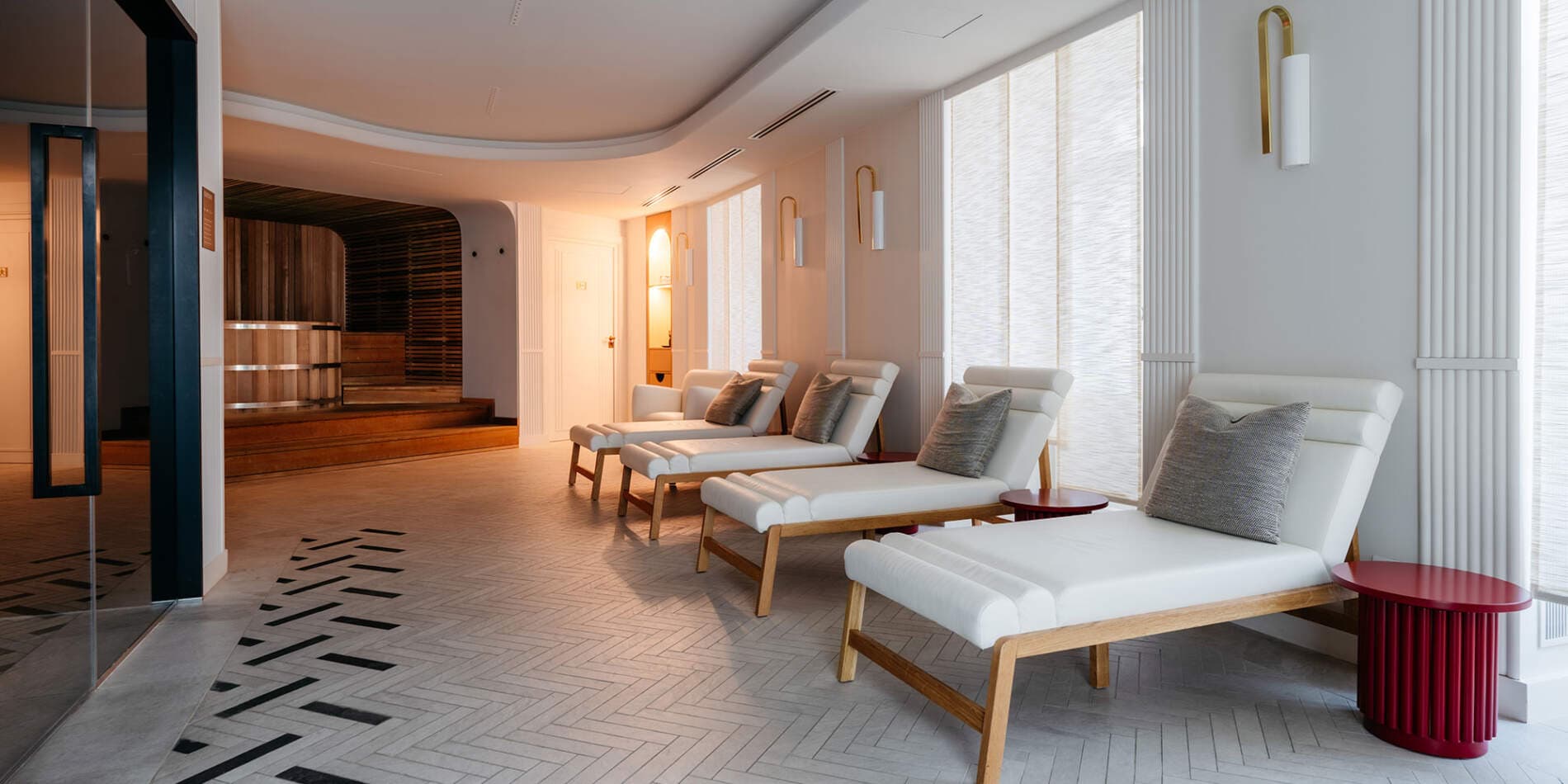 L'espace de repos du spa de la Maison Rouge à Strasbourg, ses transats blancs alignés devant les fenêtres et l'entrée en bois du sauna