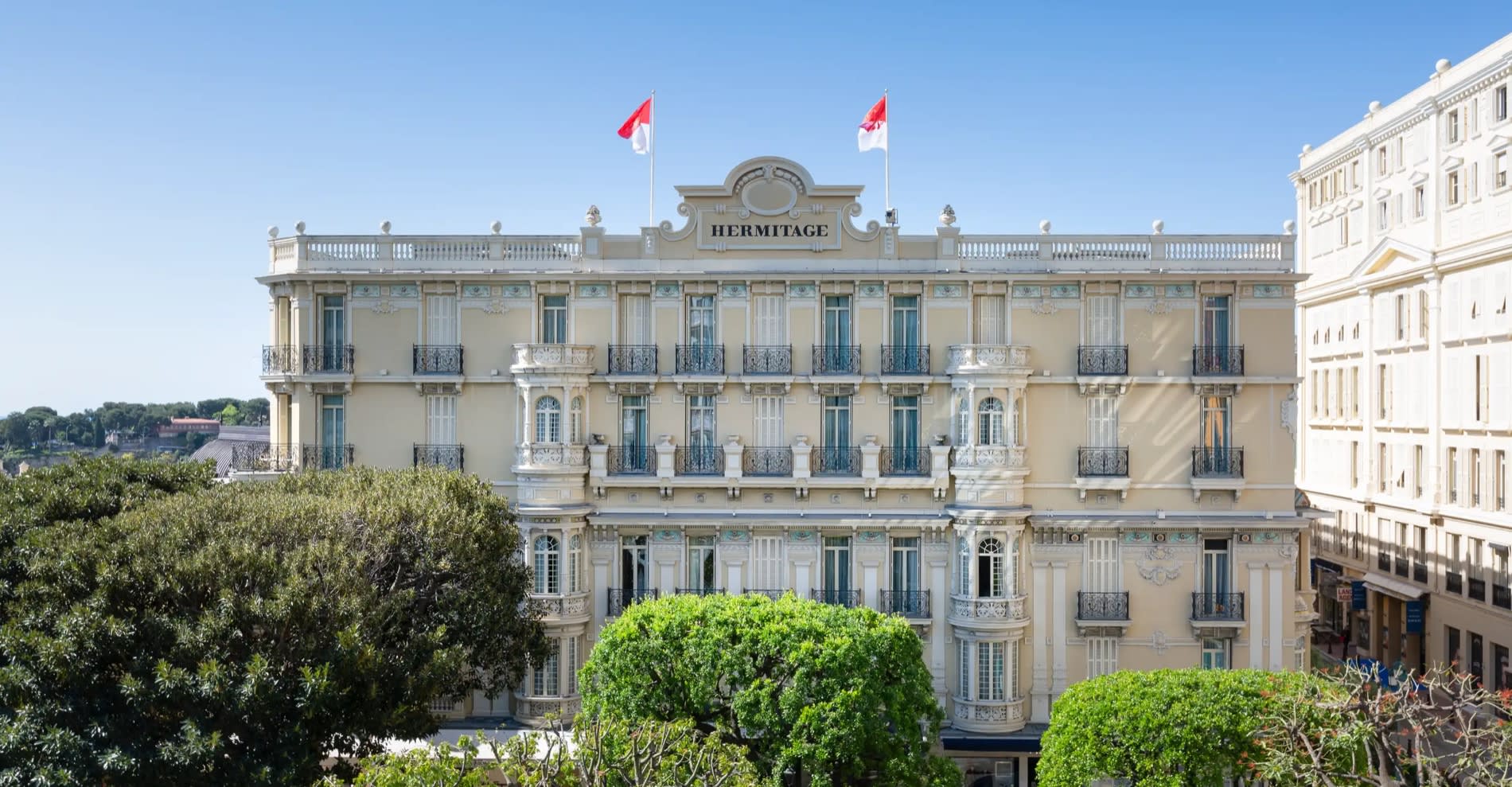 The Belle Époque facade of the Hôtel Hermitage Monte-Carlo, with its Monegasque flags, above the port of Monaco