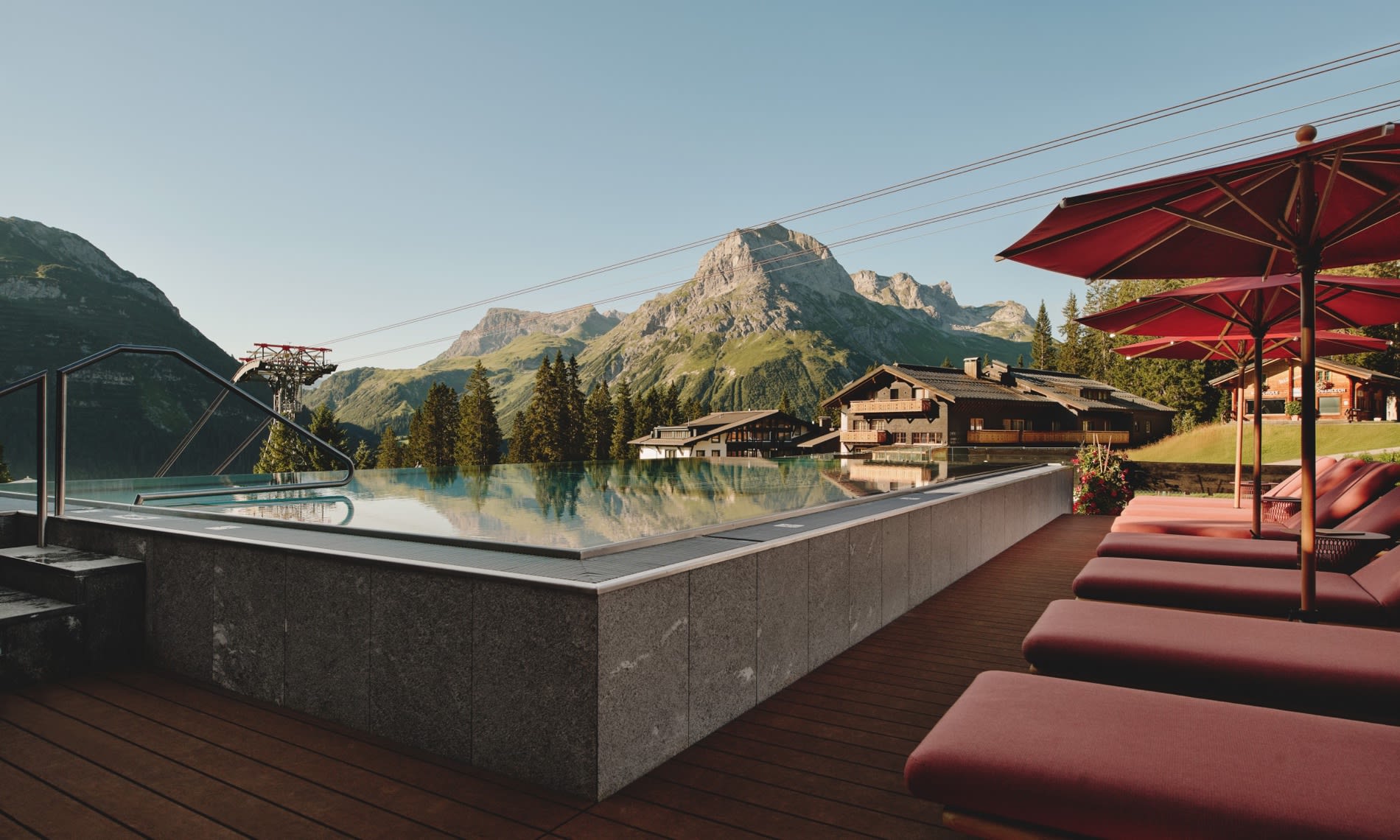 La piscina infinita del Burg Hotel Oberlech al final del día, tumbonas y sombrillas rojas, montañas del Lechtal al fondo
