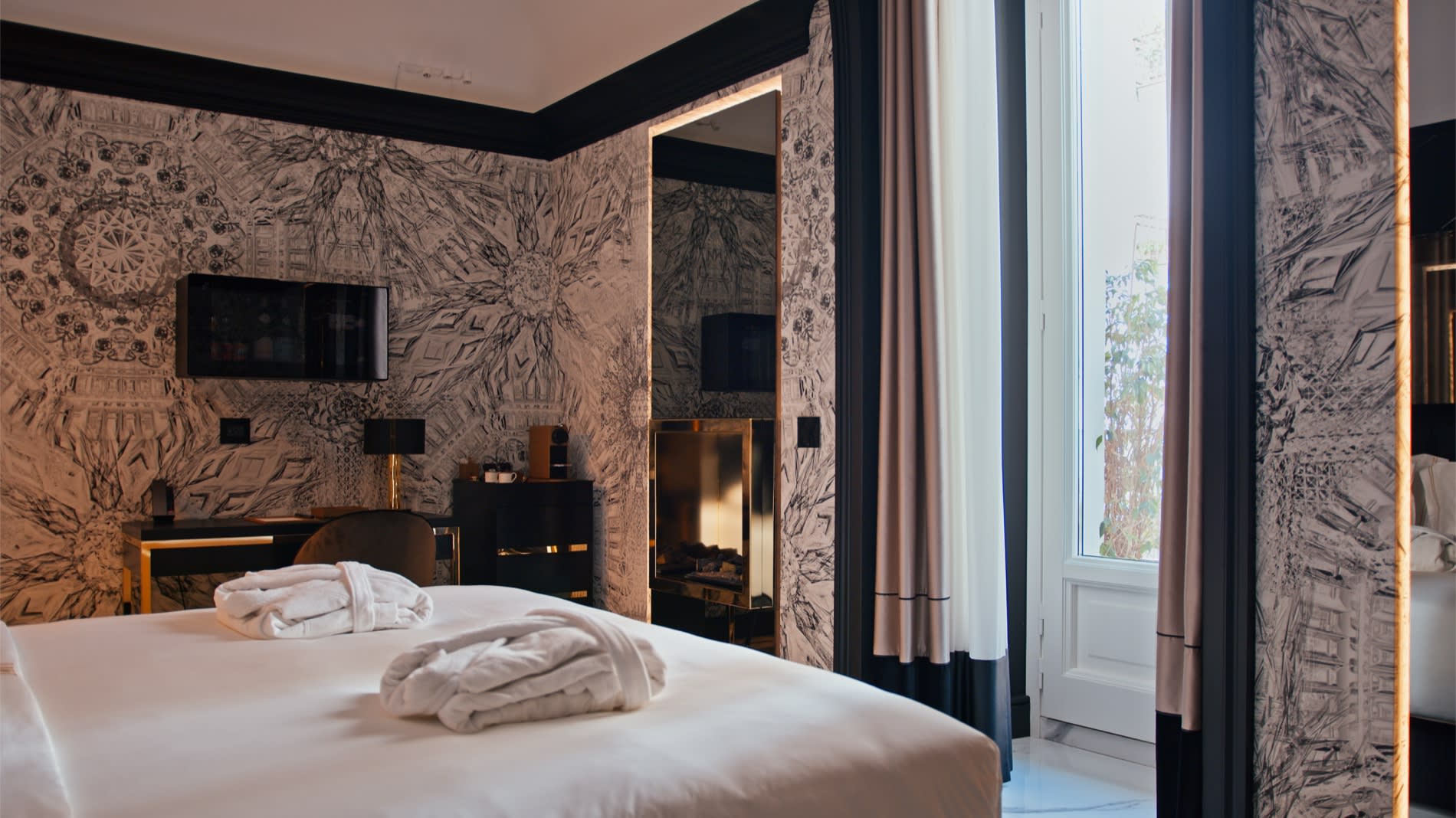 Room at the Bra Hotel in Bari, bathrobes laid on the bed, gilded mirror and tall curtained window