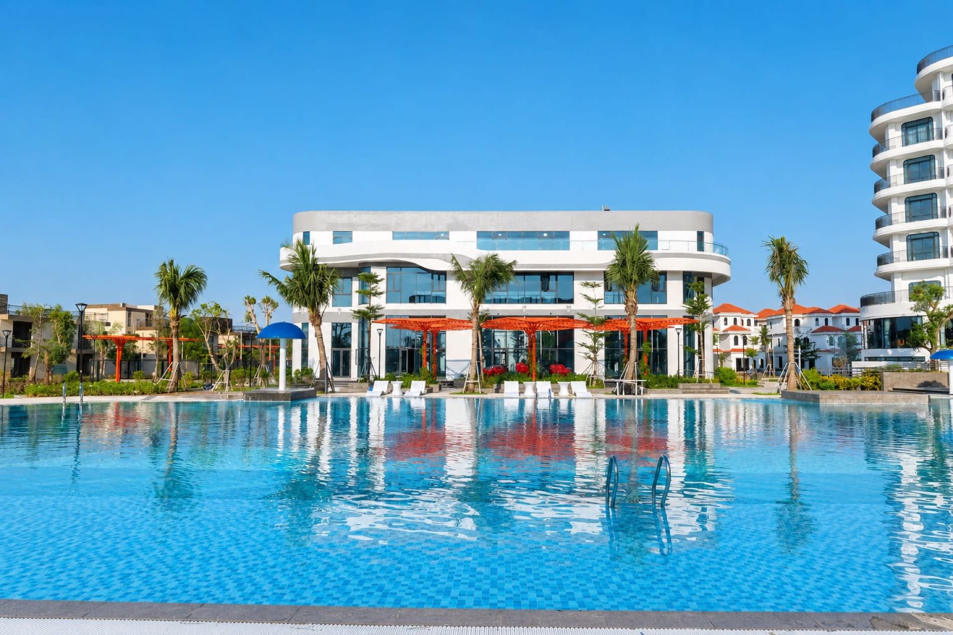 Facade blanche du Tra Co Long Beach Hotel & Resort a Mong Cai vue depuis la grande piscine exterieure bordee de palmiers