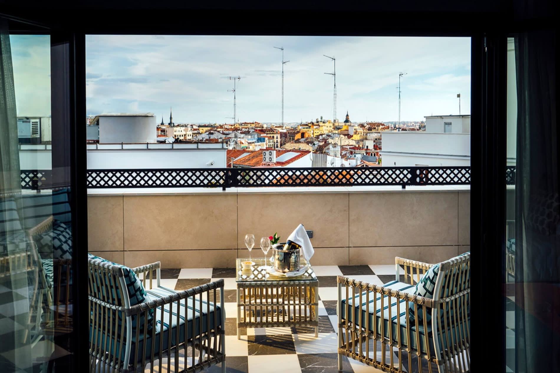 Terrasse privative vue depuis l'interieur d'une chambre de Casa Verbena Madrid, fauteuils en rotin, seau a champagne et toits de Madrid au fond