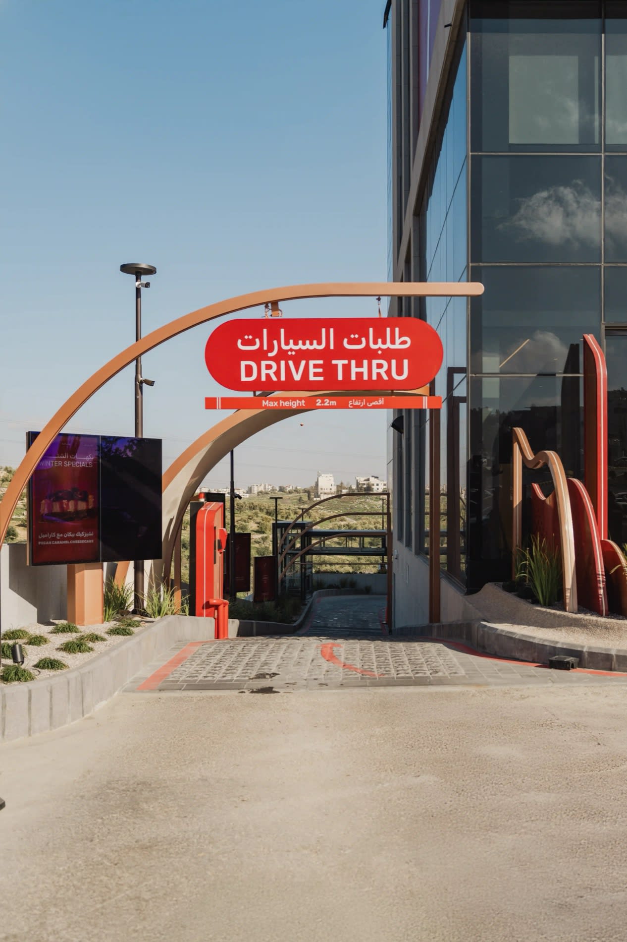 Marquesina del drive-thru de la Al Ameed Coffee Experience en la carretera del aeropuerto de Ammán, colinas al fondo