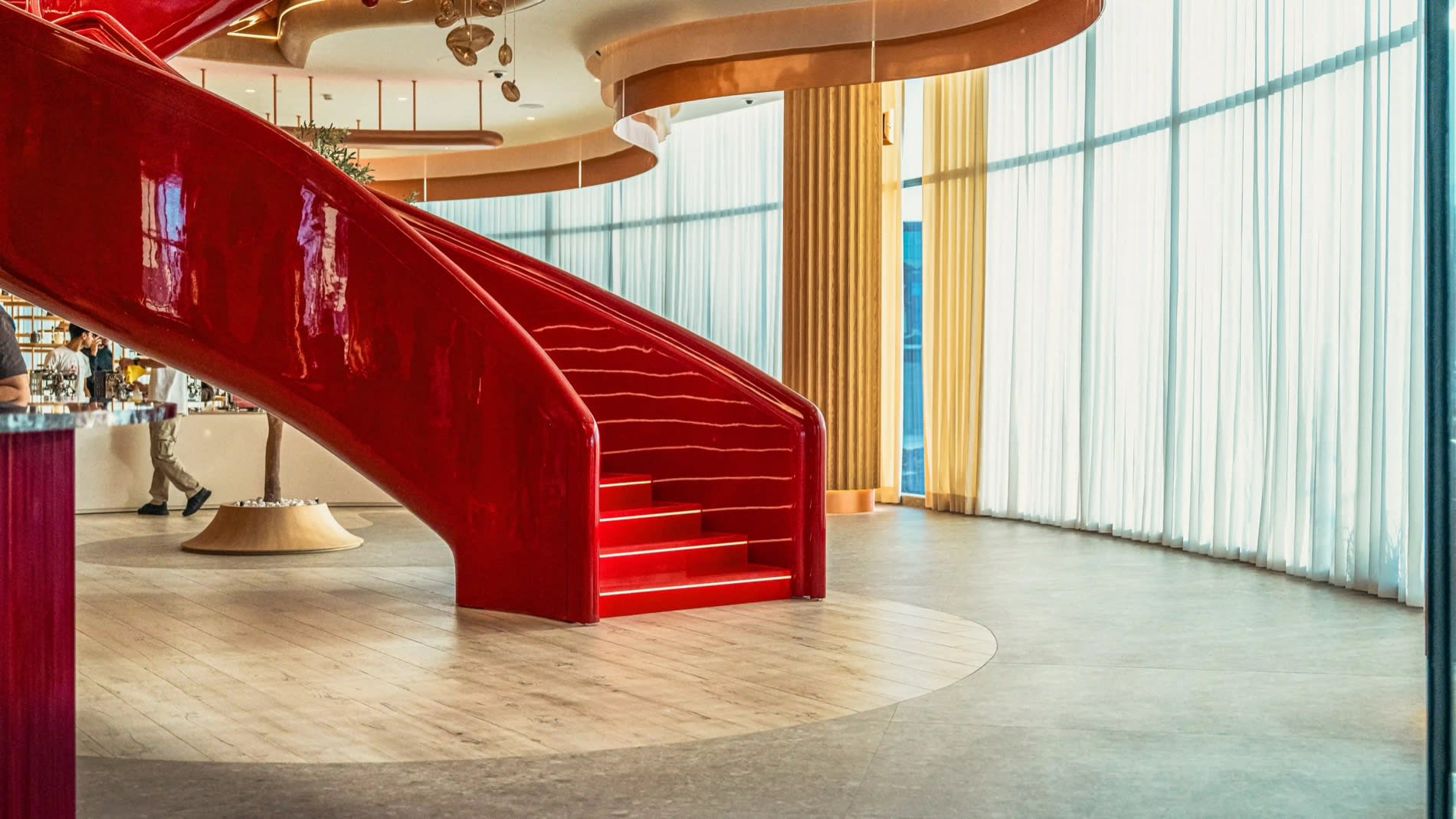 Escalera helicoidal roja lacada de la Al Ameed Coffee Experience de Ammán ante una cortina clara