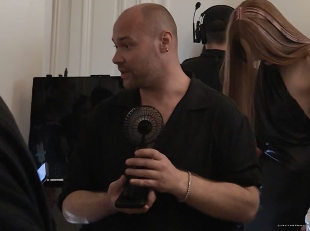 Behind the scenes at the Peet Dullaert show, a team member offers a fan