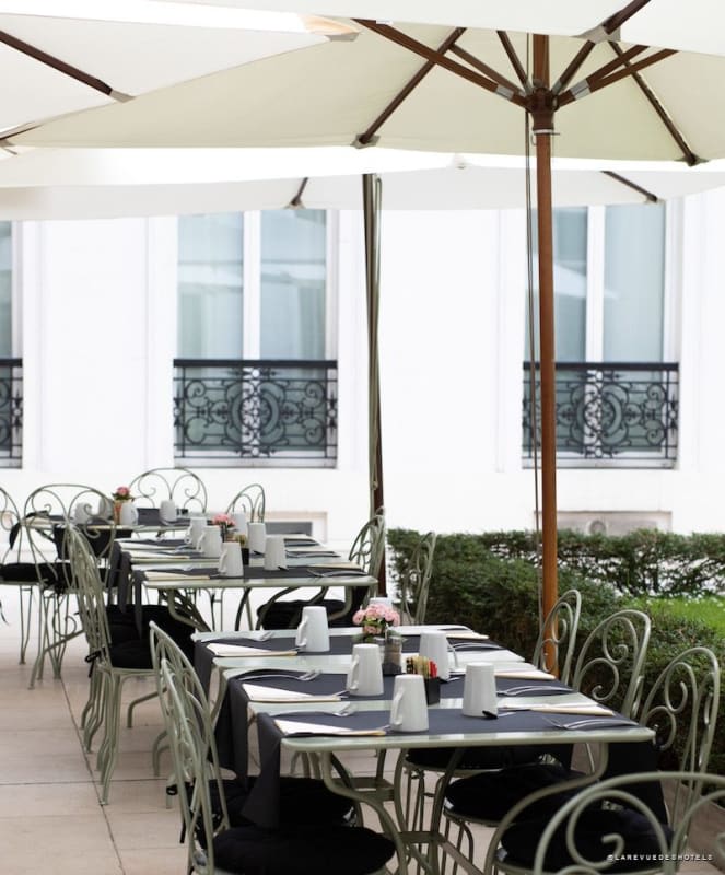 Historic hotel courtyard with a circular ivy-covered fountain statue and wrought-iron tables and chairs on a green lawn.