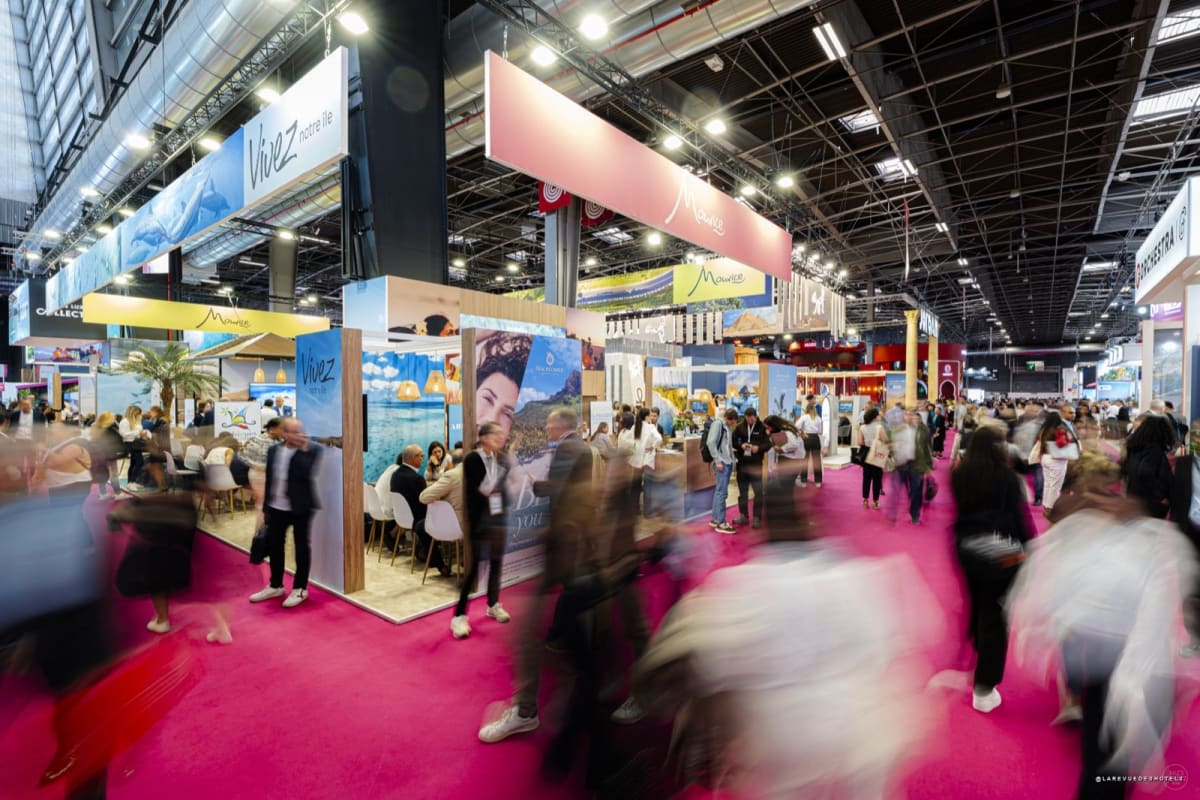 Busy exhibition hall with orange Selectour banners, pink carpet, and attendees visiting travel booths.
