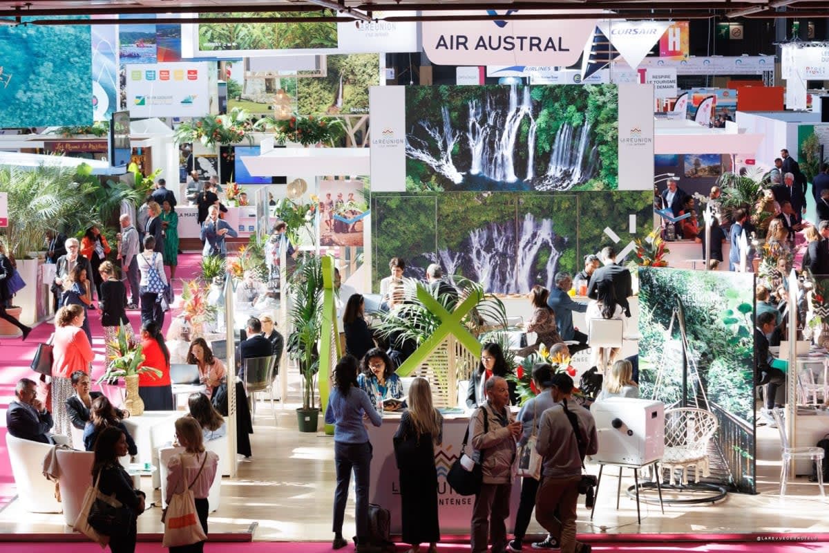 Busy exhibition hall with orange Selectour banners, pink carpet, and attendees visiting travel booths.