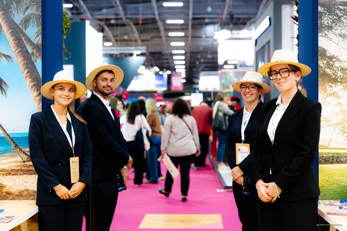 Busy exhibition hall with orange Selectour banners, pink carpet, and attendees visiting travel booths.