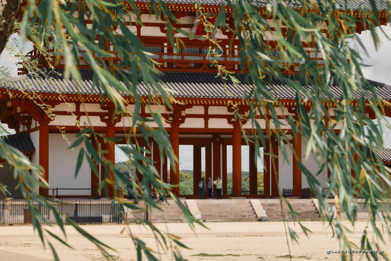 Un temple japonais aux colonnes rouges aperçu à travers des feuilles de saule