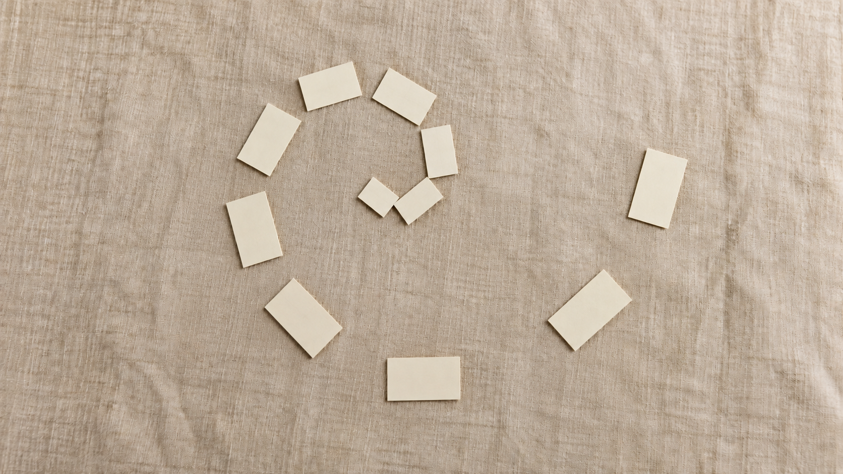 Cream index cards arranged in a widening spiral on a linen surface, each card set further apart than the last