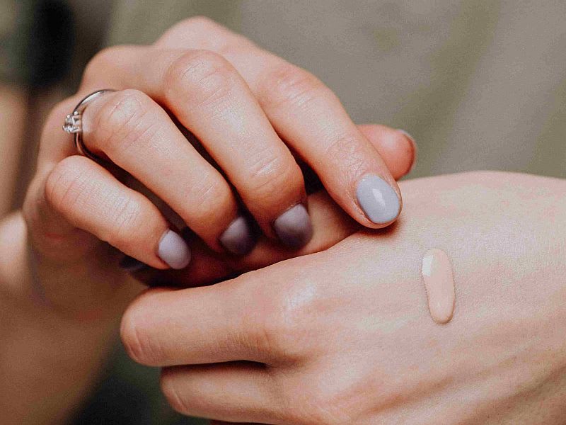 Femeie aplicând fond de ten natural pe față, machiaj subtil, lumină naturală