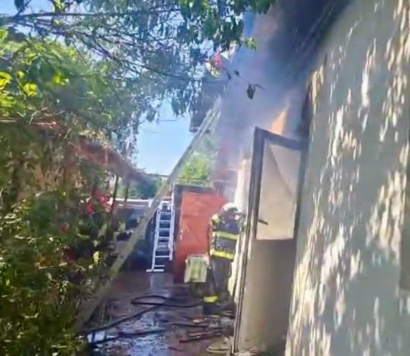 Pompieri români intervenind la incendiu, victimă scoasă din casă