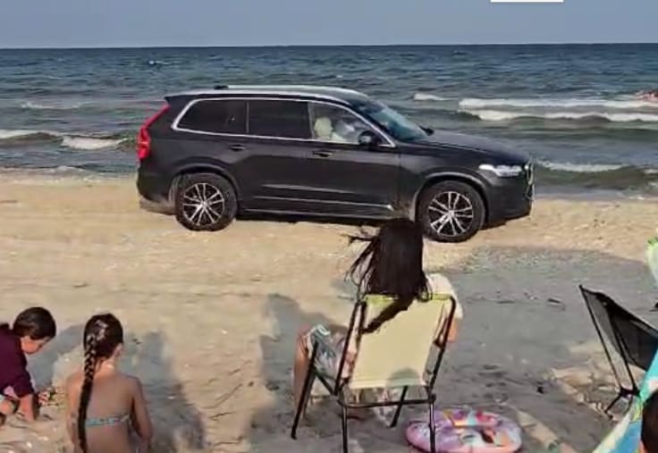 Mașină circulând pe plaja din Vadu, turiști pe fundal Mașină circulând pe plaja din Vadu, turiști pe fundal