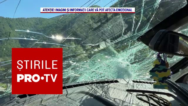 Mașină avariată sub un versant abrupt, cu bolovani căzând peste drum, zona împădurită din România
