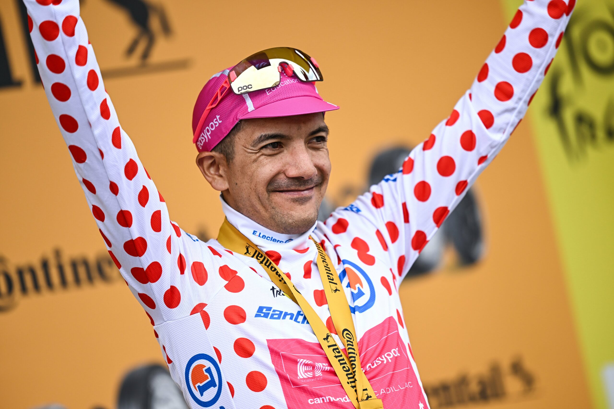 Richard Carapaz în tricou alb cu buline roșii pe bicicletă în munți