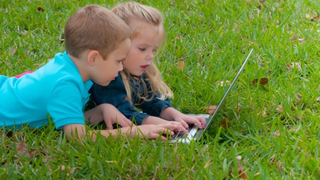 copii lucrând la laptop pe iarbă