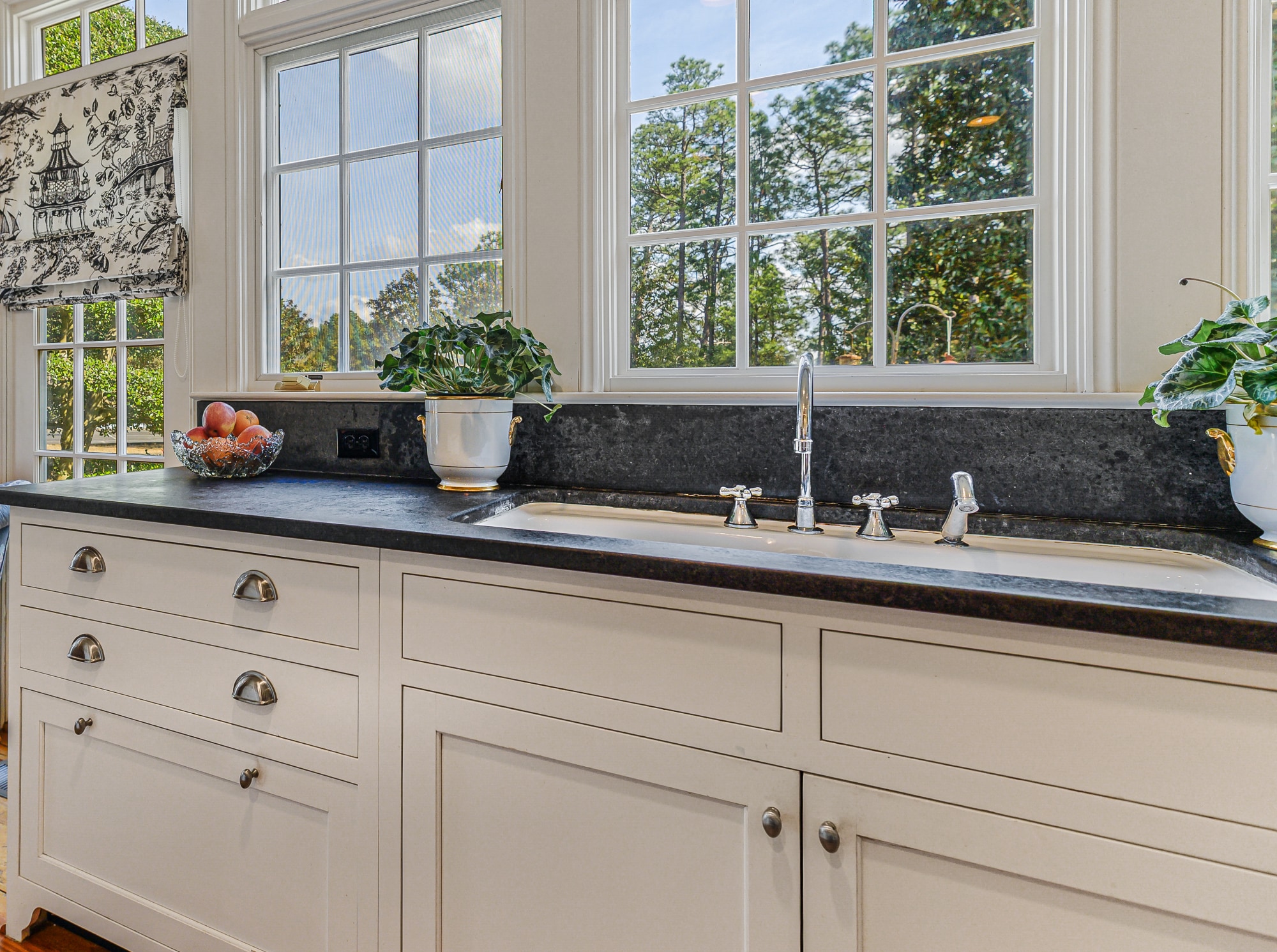 The wall of windows over the sink — black granite, white cabinetry, the pines beyond