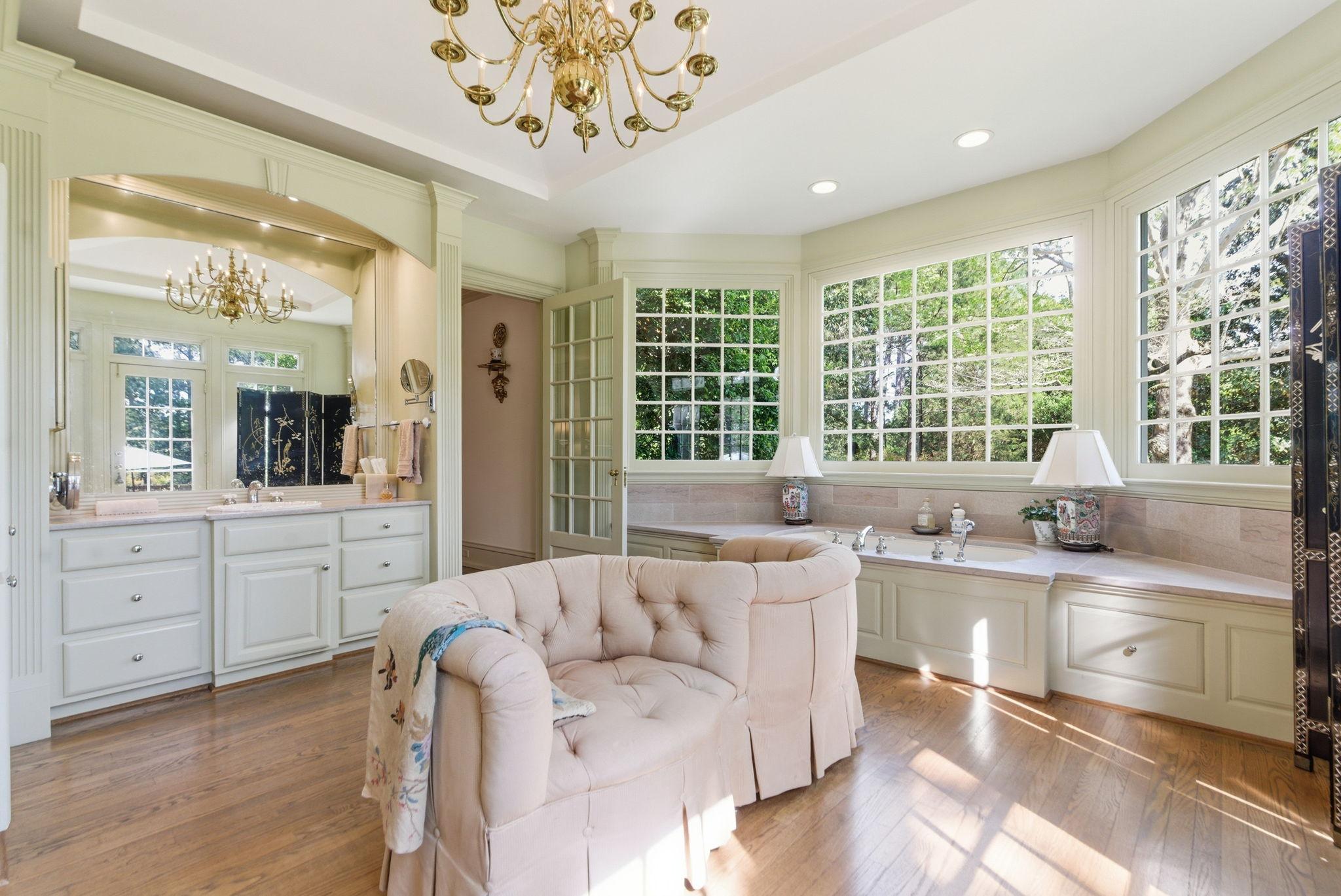 Garran Hill mirror bath — gold chandelier, built-in tub under windows, greenery views