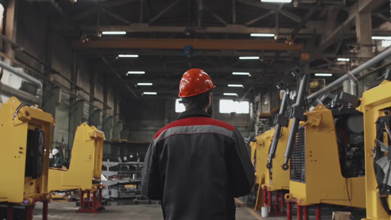 Mitarbeiter mit rotem Schutzhelm geht durch eine Produktionshalle mit gelben Maschinenrahmen.