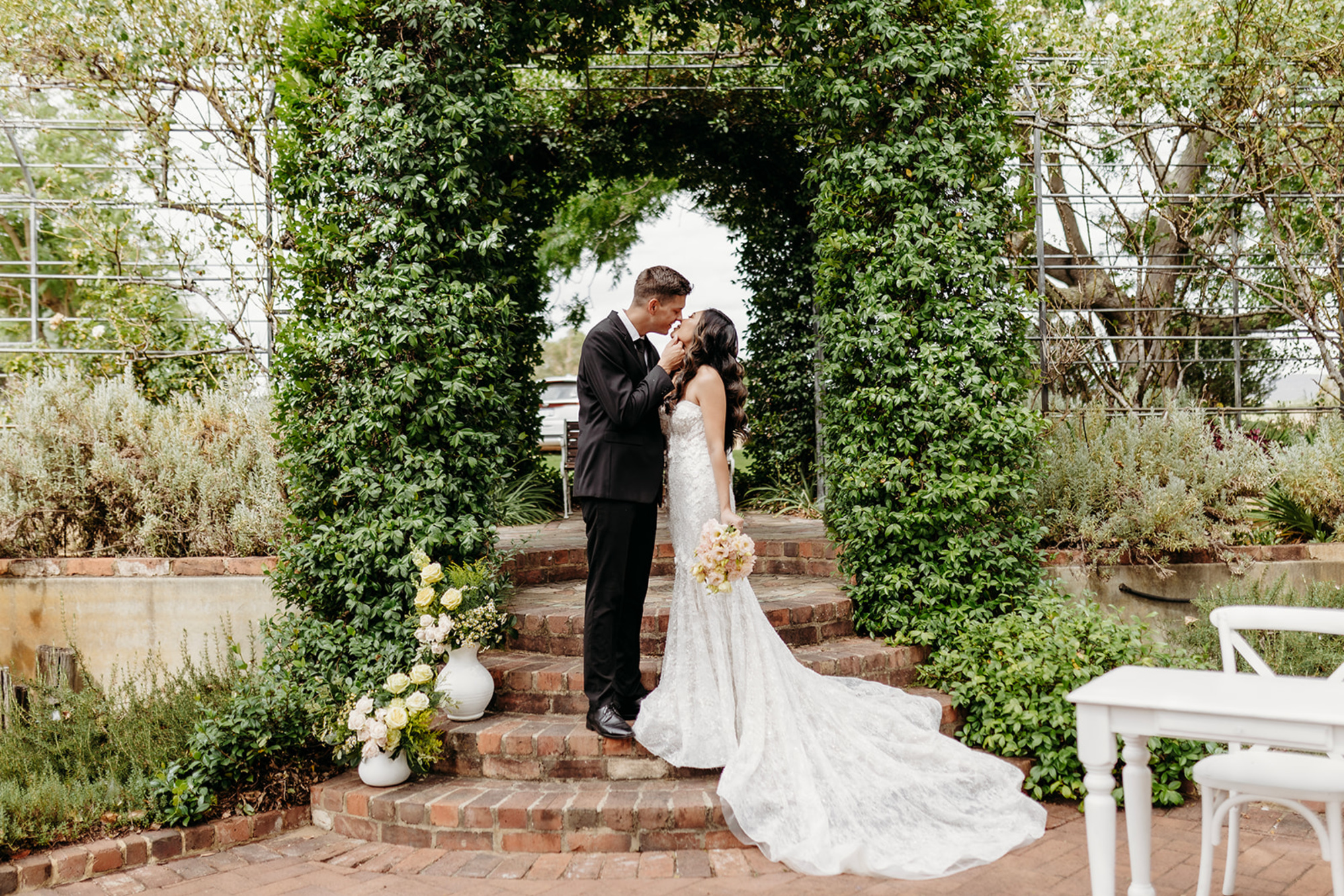 A loving couple shares a kiss under a lush green archway, perfect for an intimate garden wedding.