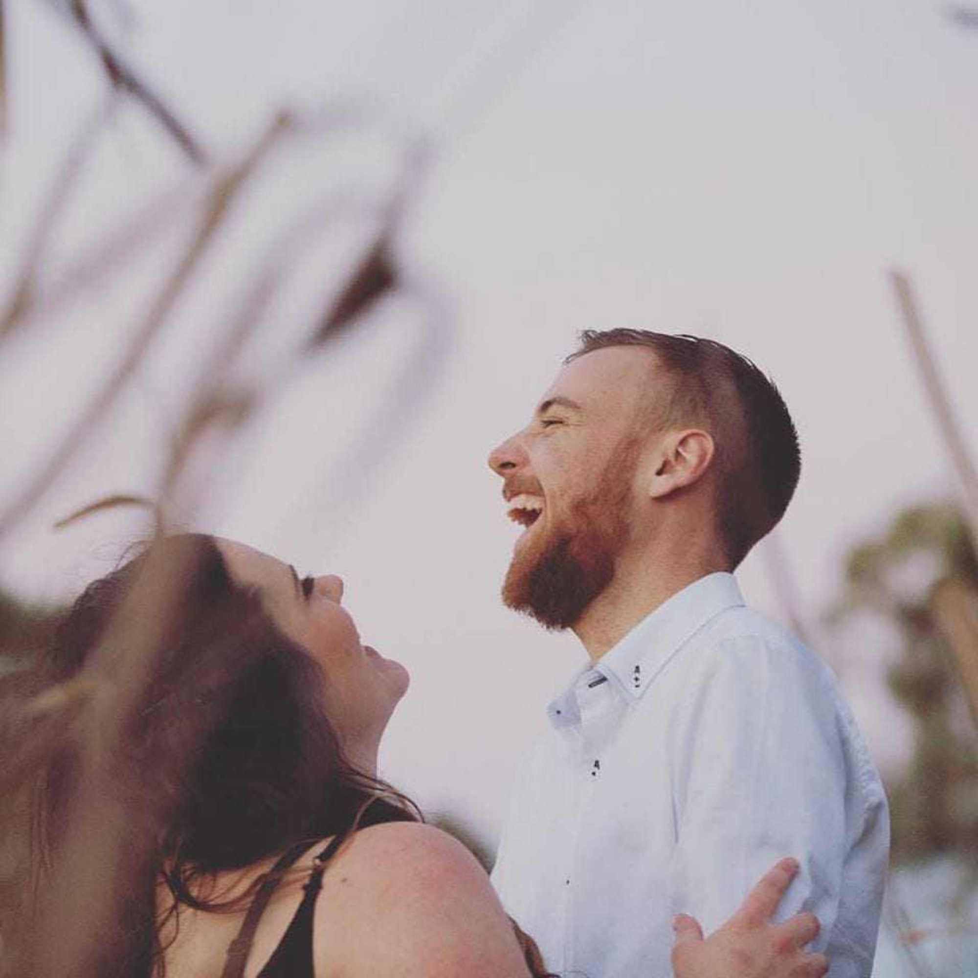 Smiling couple share a joyful laugh together outdoors in soft natural light.