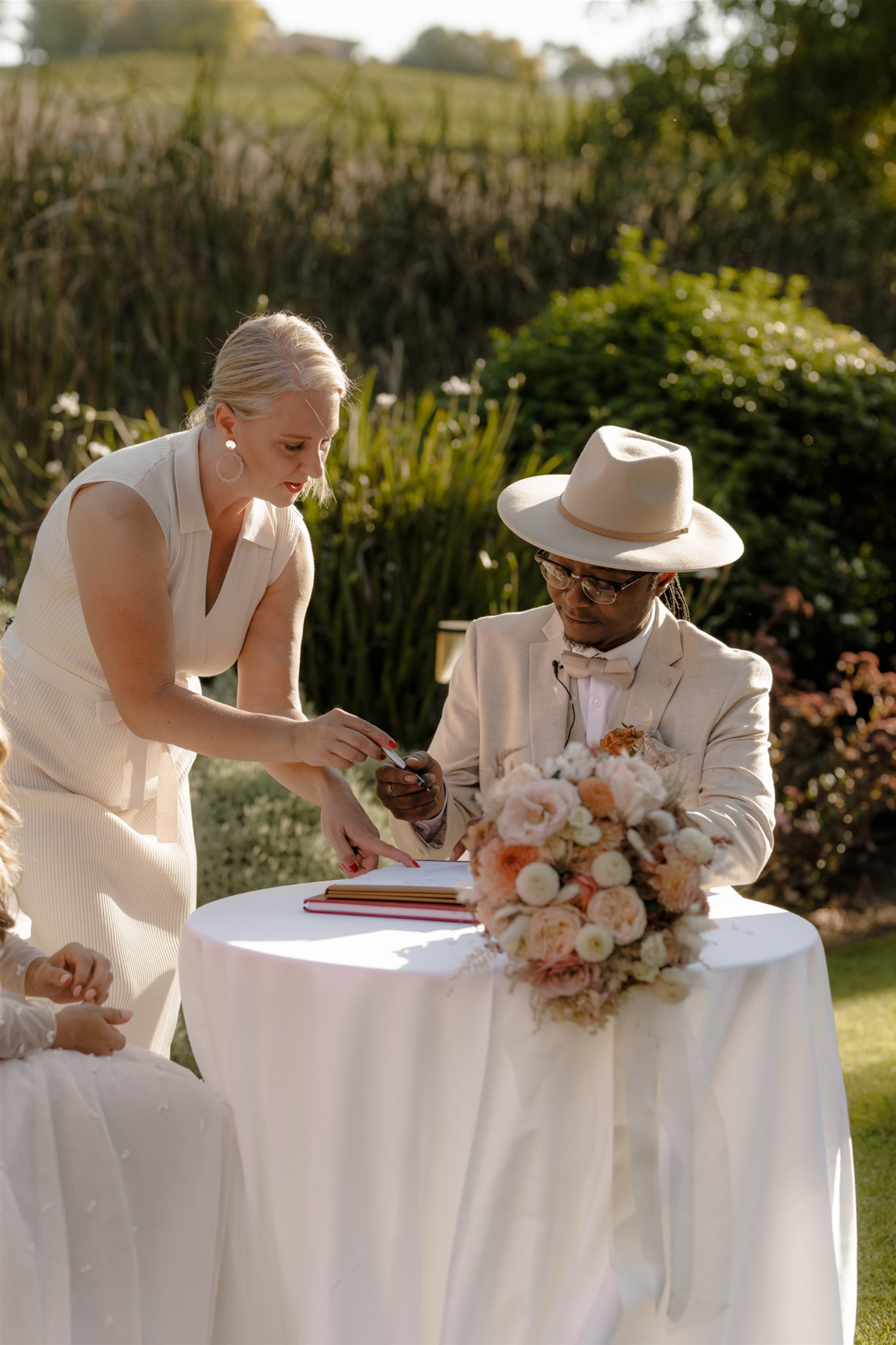 Outdoor wedding ceremony where a couple signs the marriage register at a round table with a blush bouquet.