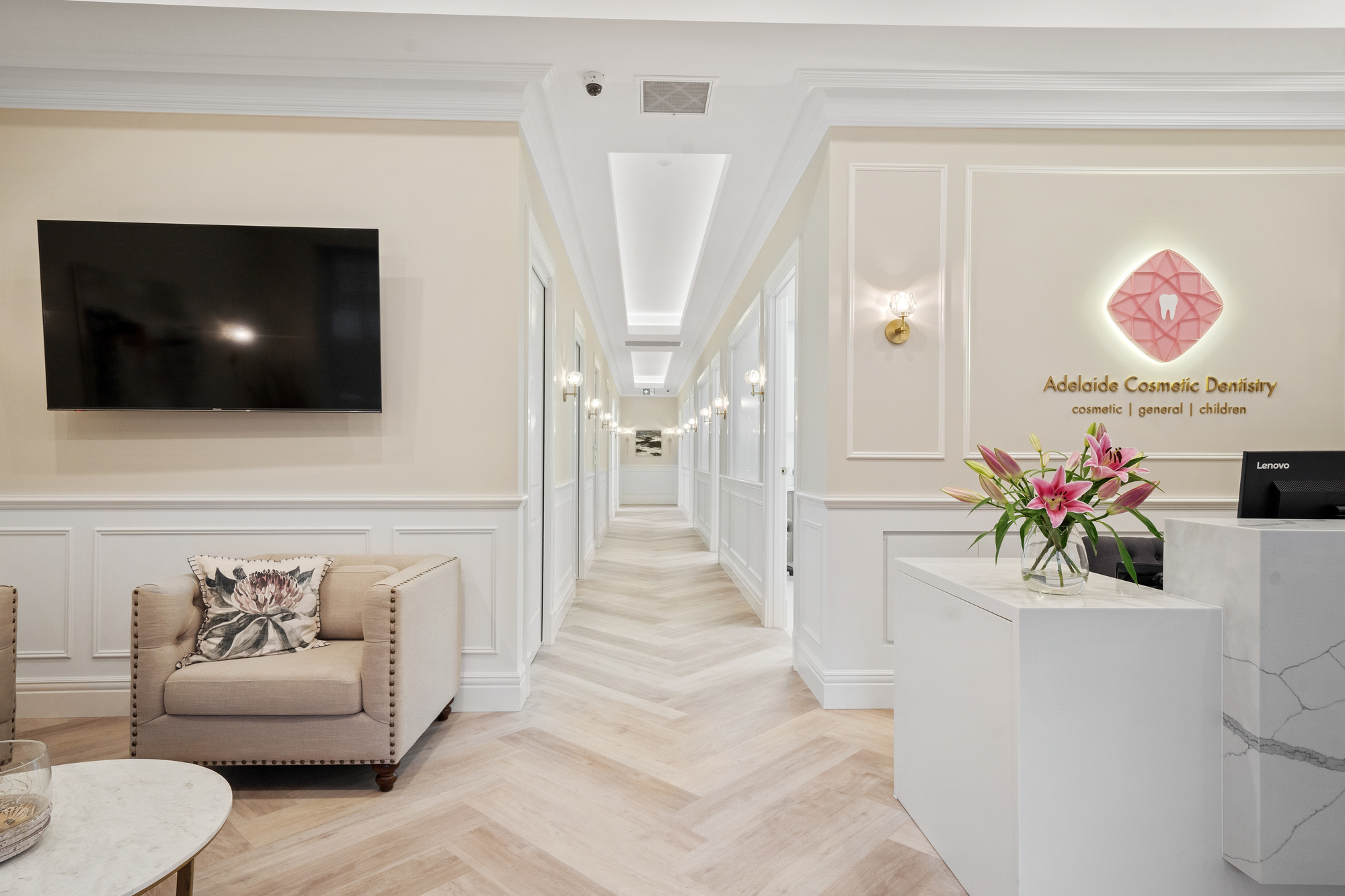 Elegant modern reception lounge and hallway with neutral decor and fresh pink lilies on the counter.