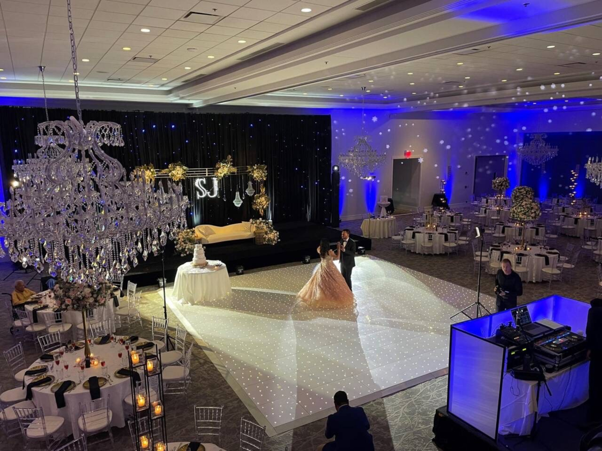 Luxurious ballroom wedding reception with chandeliers and a couple sharing their first dance on a sparkling white floor.
