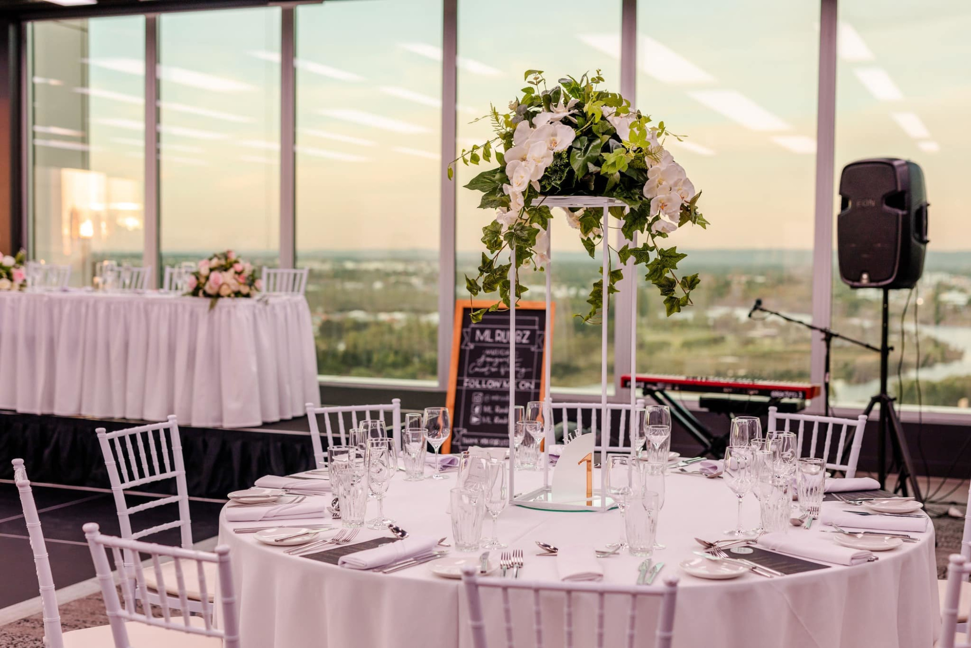 Elegant wedding reception setup with floral centerpiece and city views through large windows.