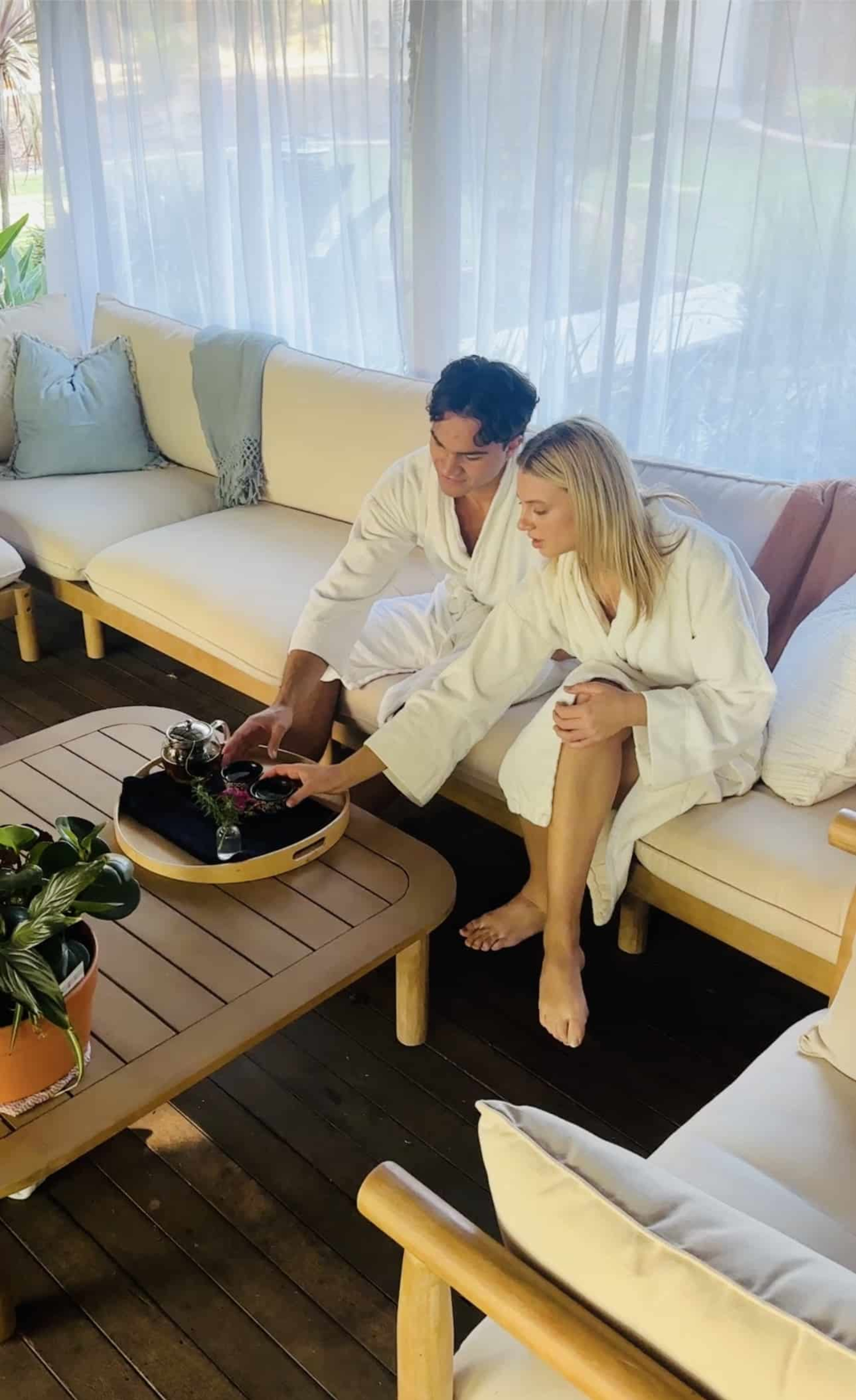 Couple in white robes relaxing with tea in a cozy lounge area with soft seating and natural light.