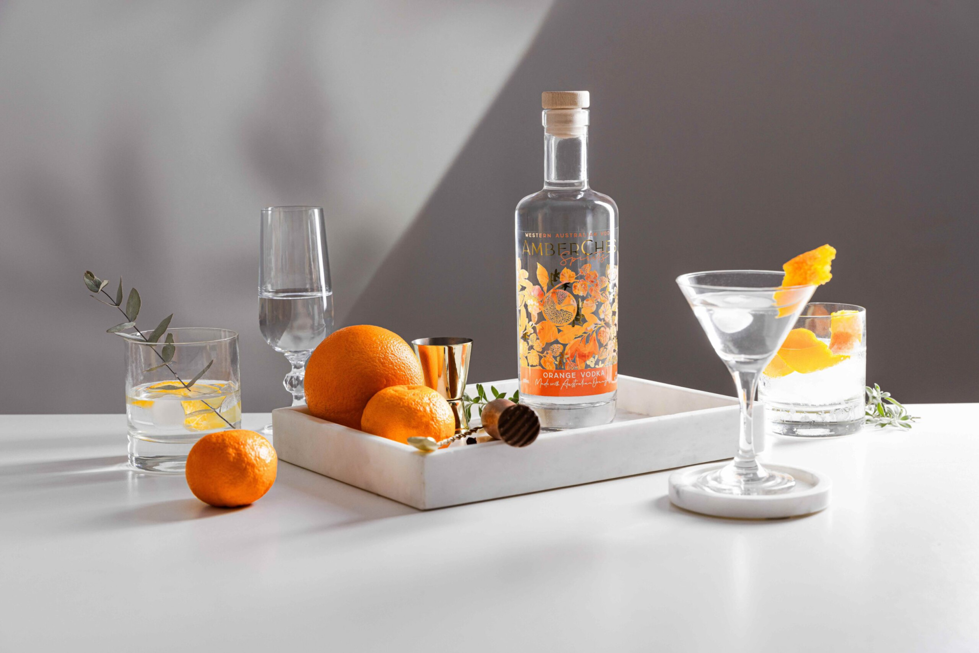Stylish orange vodka cocktail display with fresh oranges and glassware on a white tray.