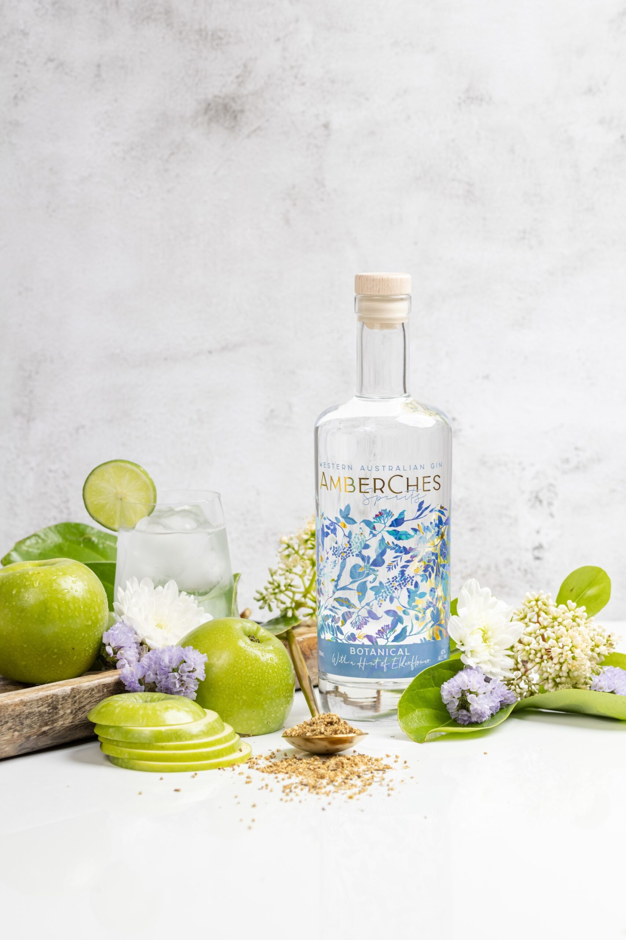 Botanical gin bottle styled with green apples, flowers, and a cocktail glass on a white surface.