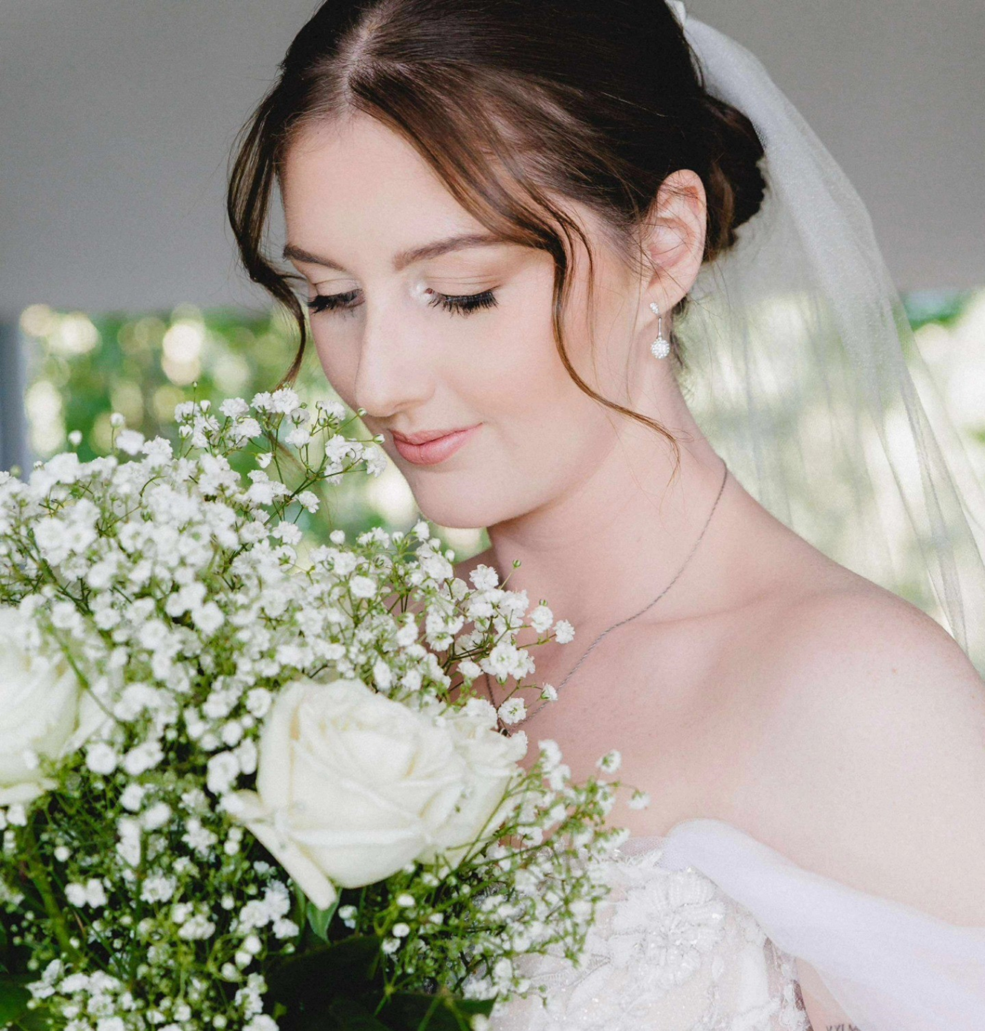 Soft bridal portrait of a bride in veil holding a large white rose and baby’s breath bouquet.