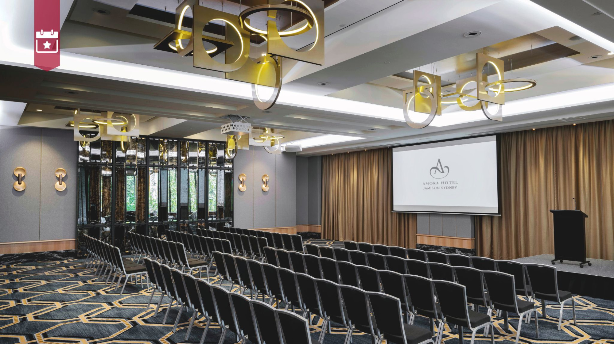 Modern hotel ballroom set with rows of chairs facing a stage and projector screen for a wedding or event.
