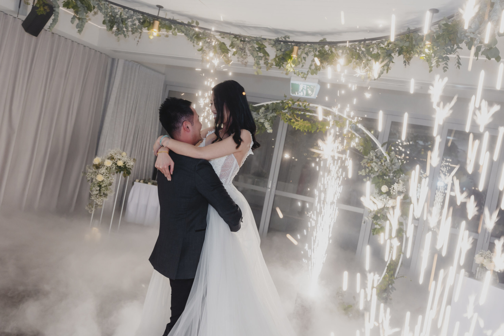 Bride and groom share a romantic first dance surrounded by indoor sparklers and soft fog.