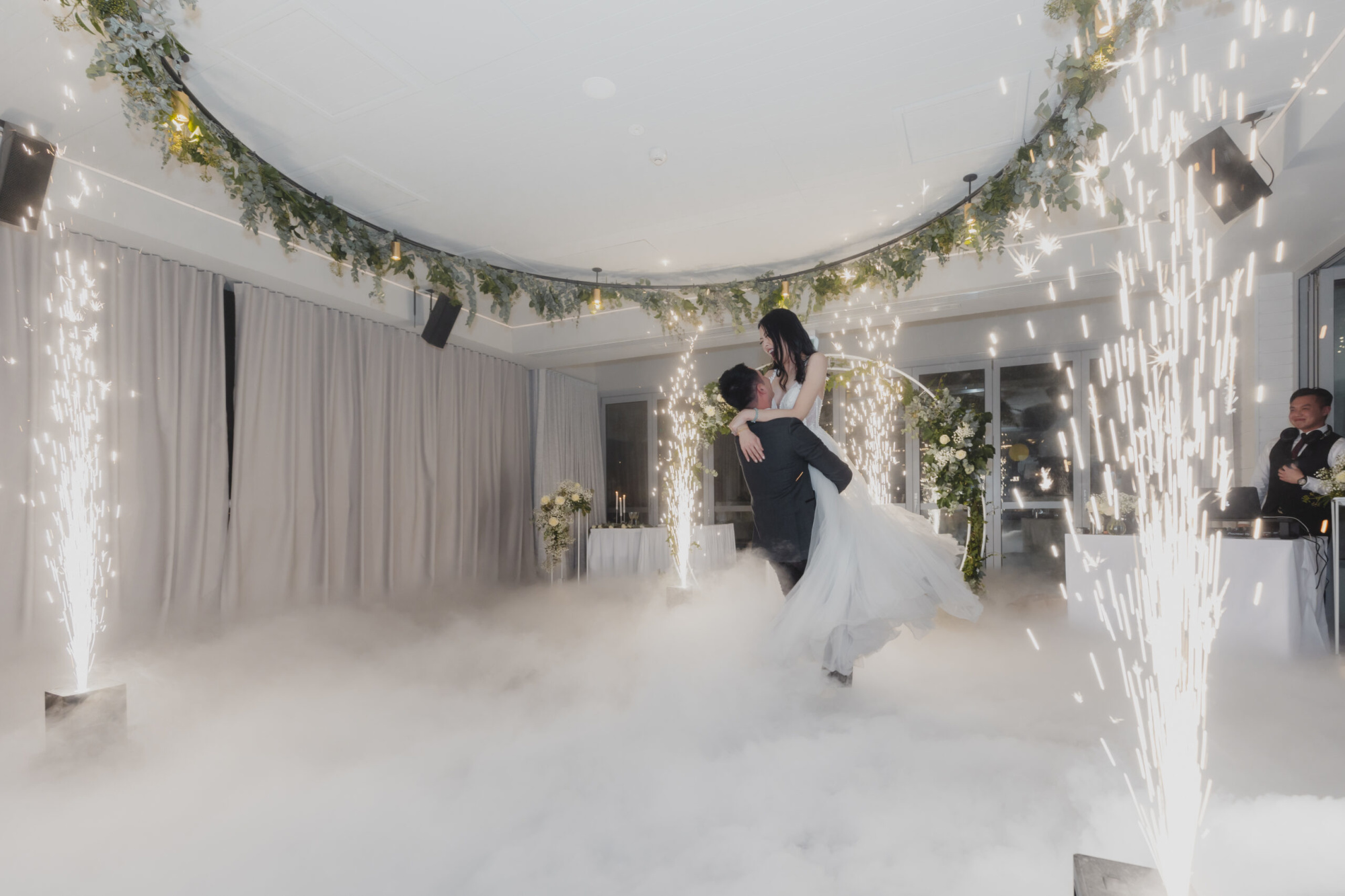 Bride and groom share a dramatic first dance amid fog and indoor sparkler fountains in an elegant reception space.