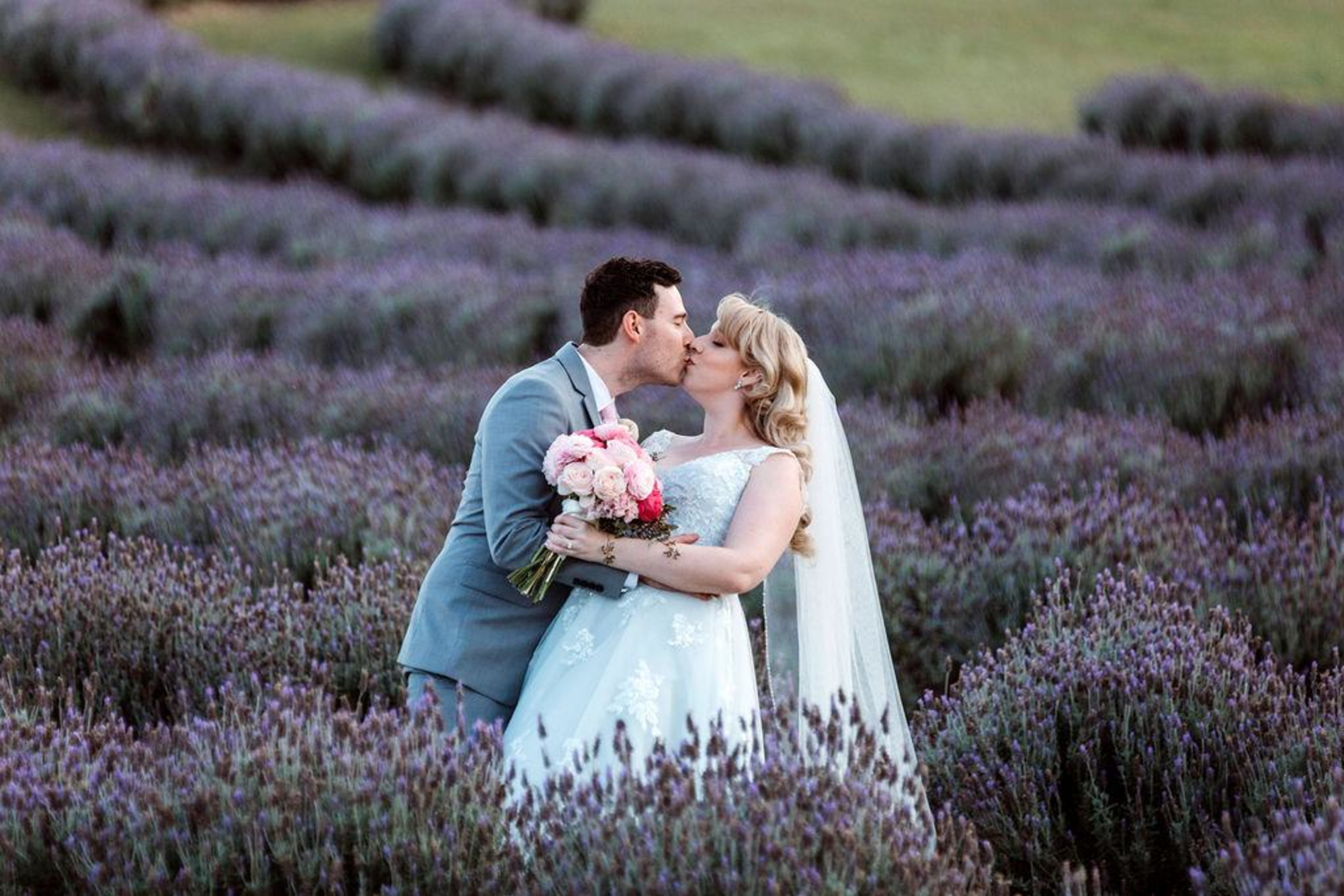 Bride and groom share a kiss while embracing in a blooming lavender field.