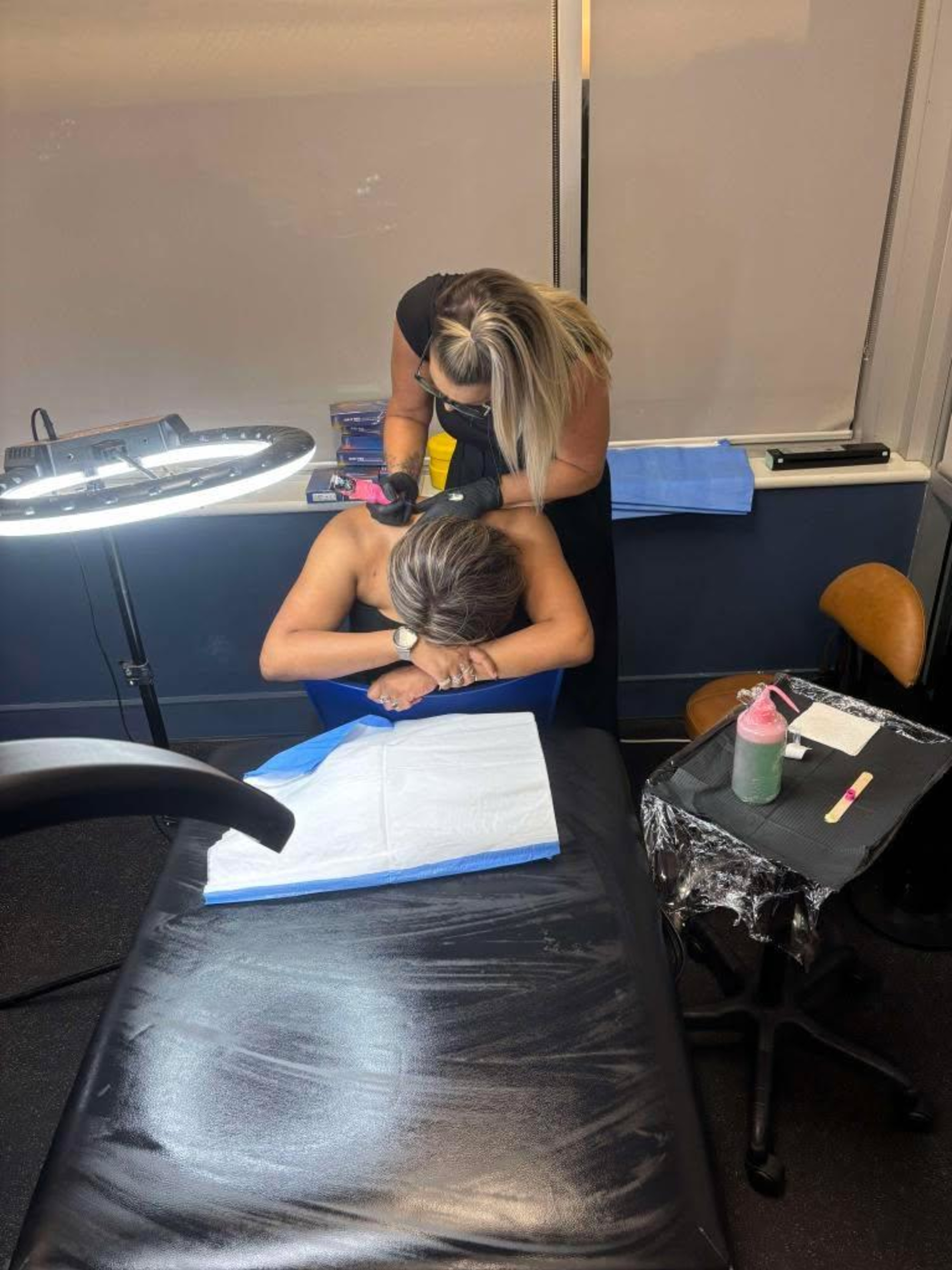 Tattoo artist working on a woman's back in a studio, viewed from above the treatment table.