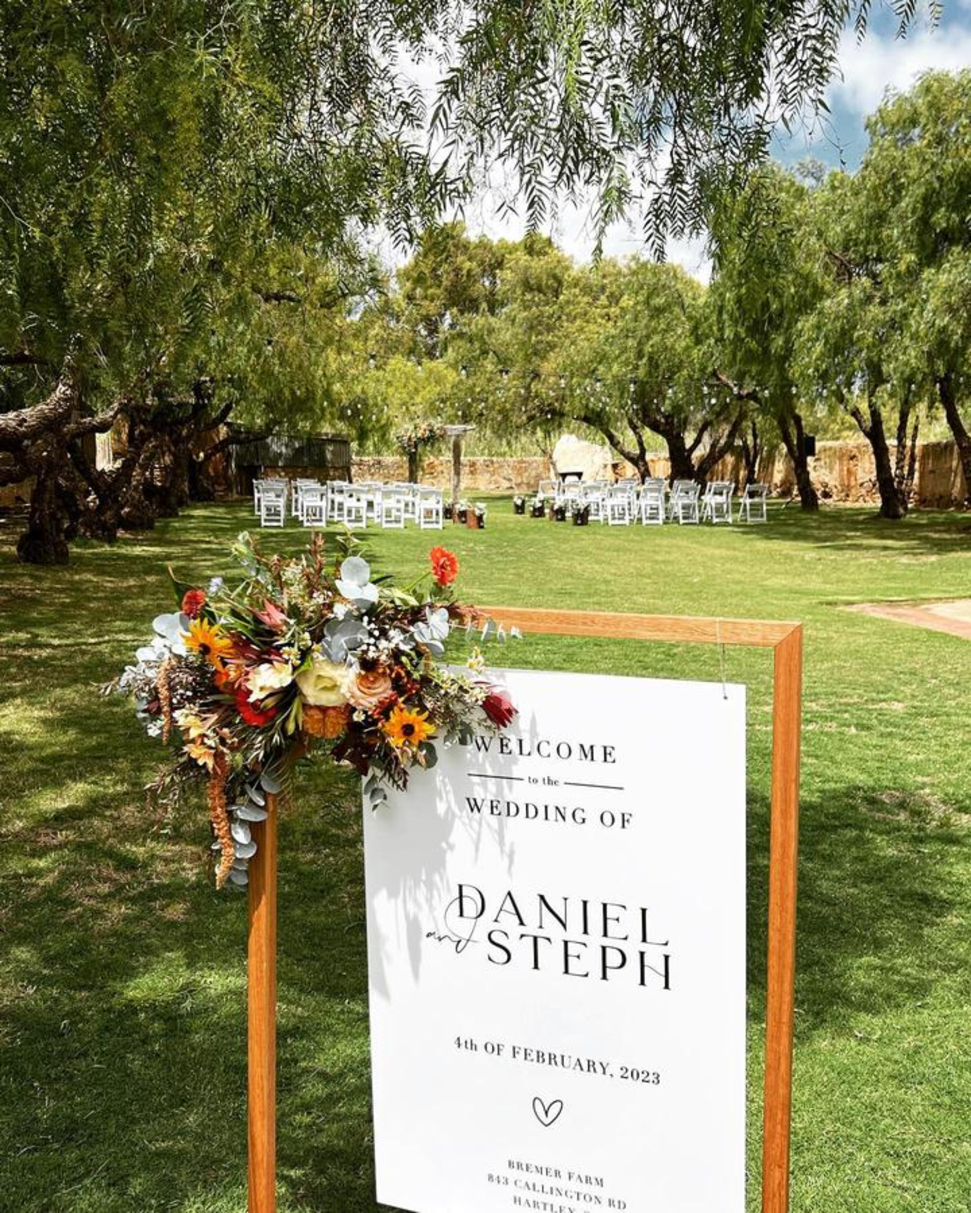 Outdoor garden wedding ceremony setup with a floral welcome sign for Daniel and Steph at a rustic farm venue.