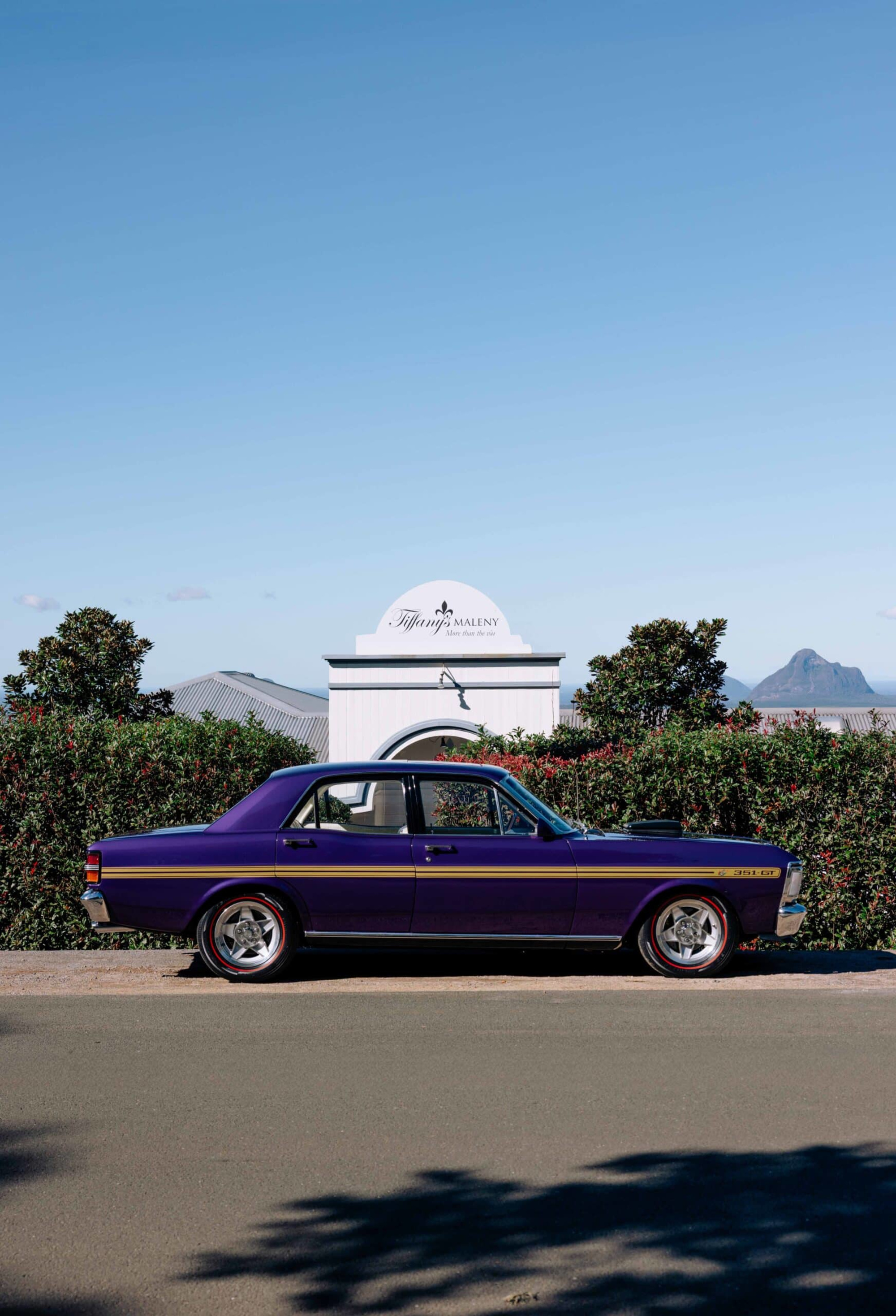 Purple classic car parked in front of a white country wedding venue under a clear blue sky.