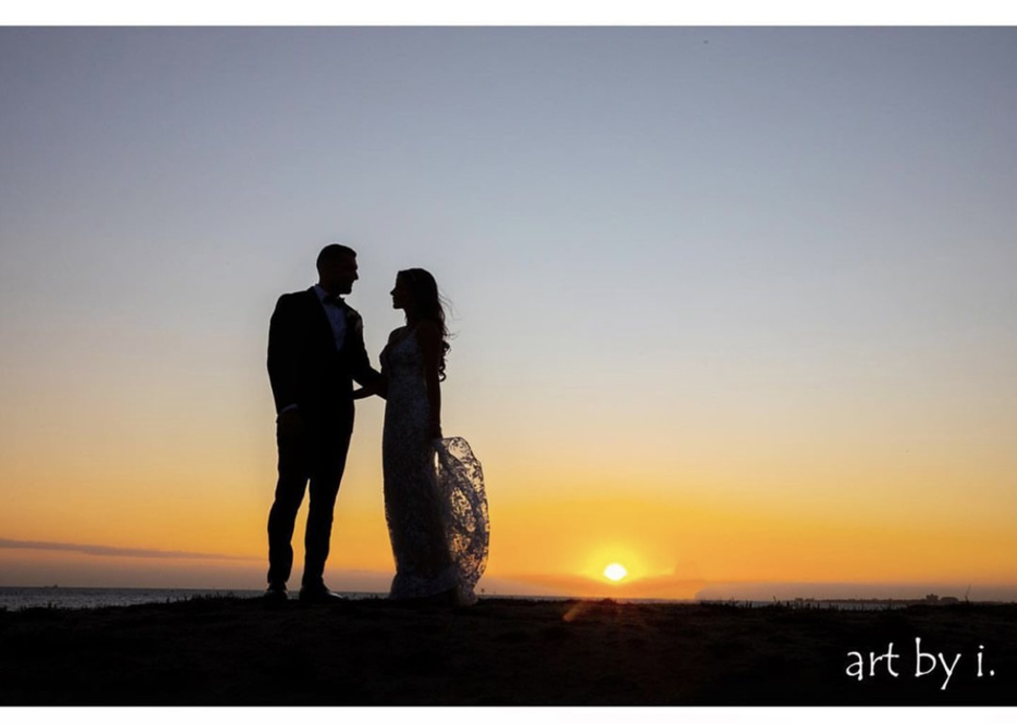Silhouetted bride and groom holding hands at sunset on a beach shoreline.