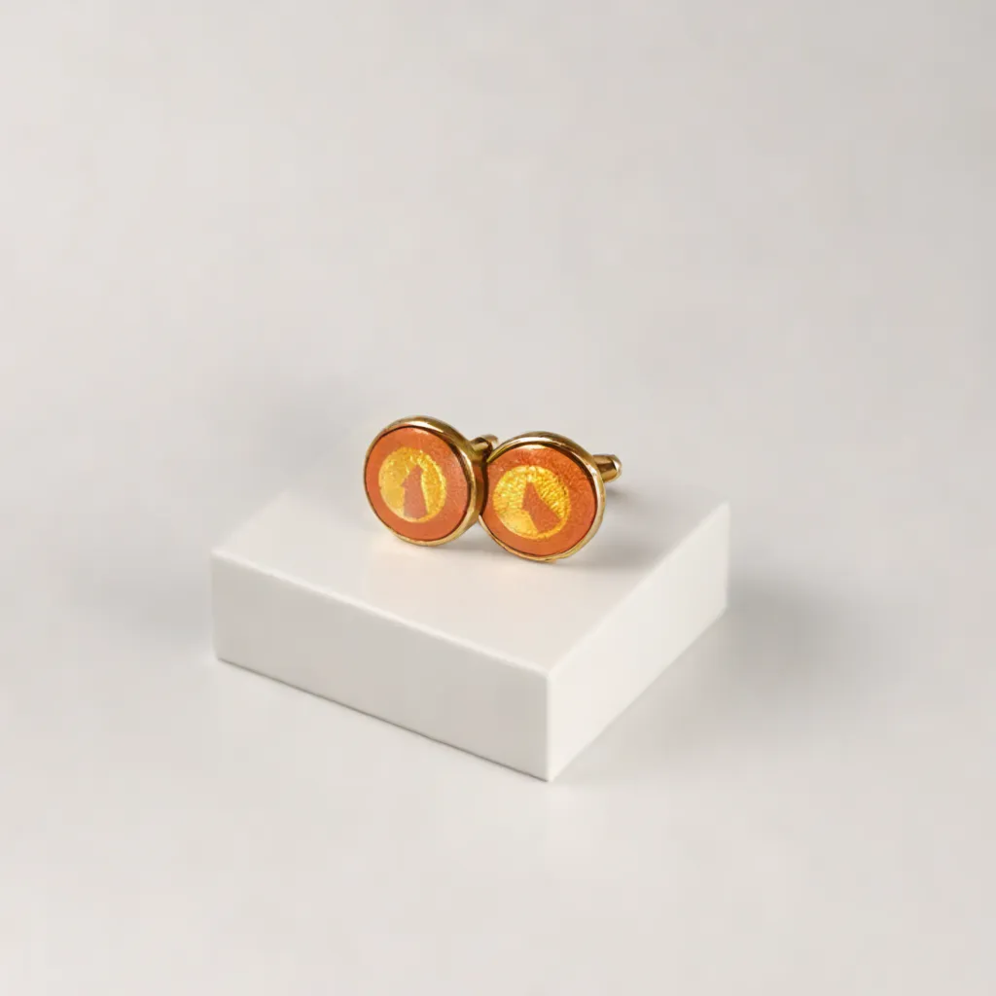 Gold and orange round cufflinks displayed on a white block against a neutral background.